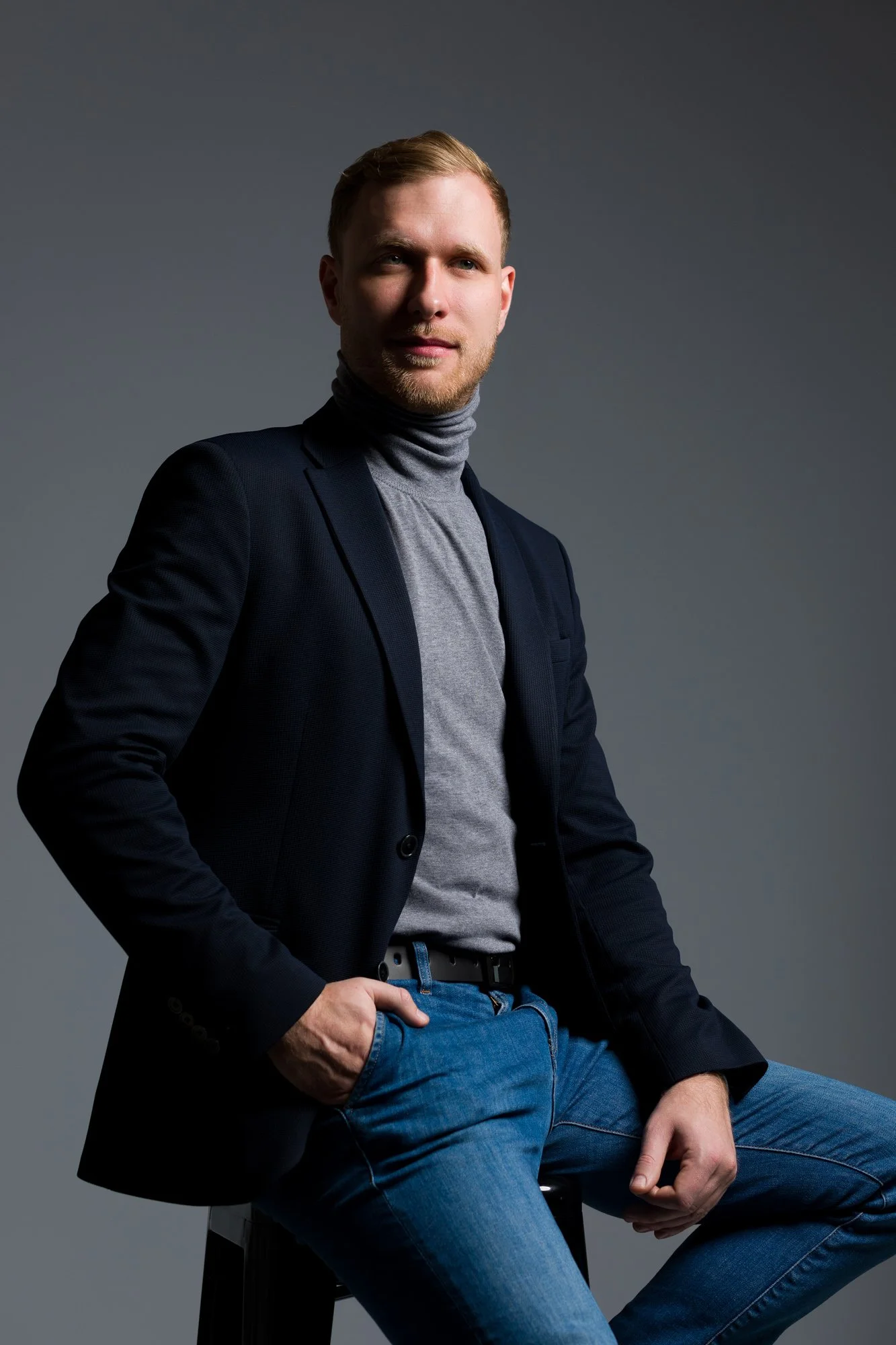 portret z bocznym światłem mężczyzny, w marynarce i szarym golfie pozuje w studio podczas sesji wizerunkowej