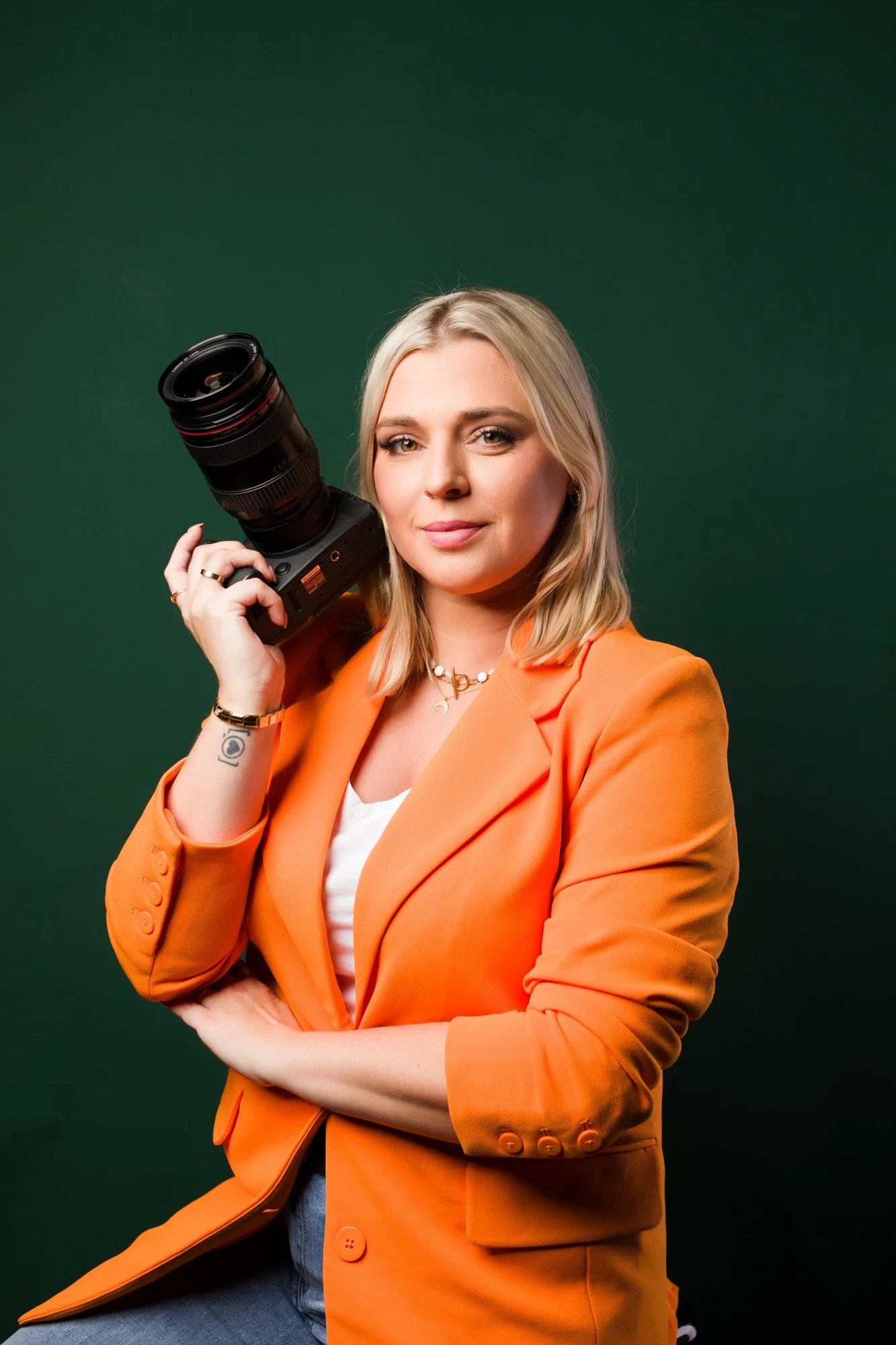 sesja wizerunkowa fotografki, z aparatem w ręce i pomarańczowym garniturze