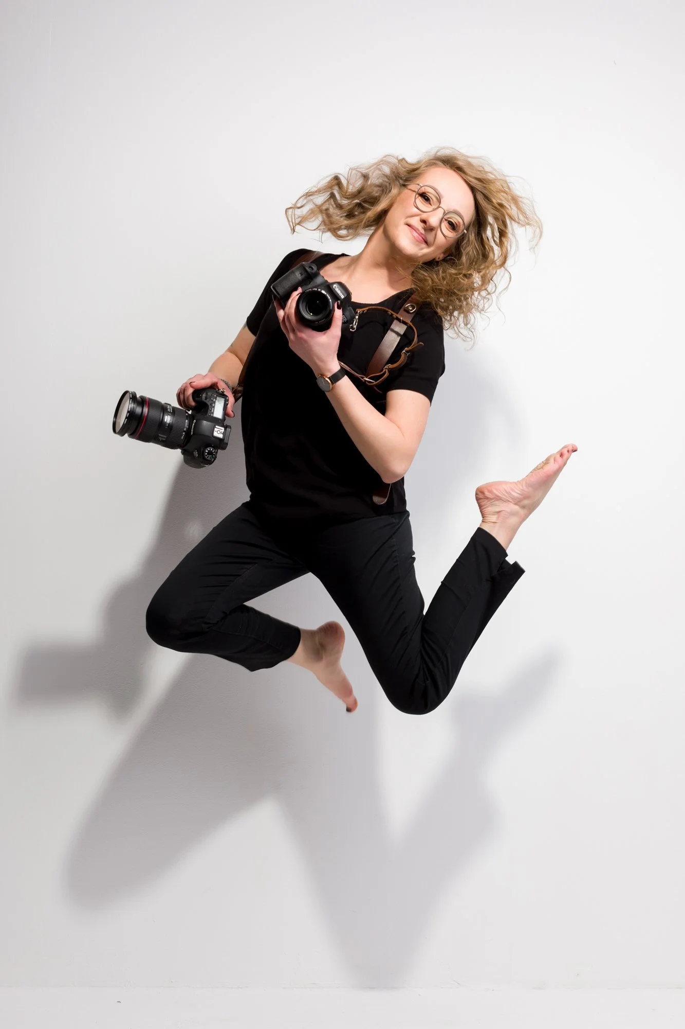fotografka kobieta, z aparatami w rękach skacze podczas sesji wizerunkowej w studio