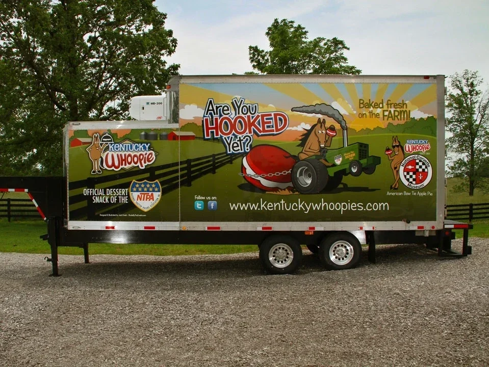 A mobile advertising trailer promoting Kentucky Whoopie, featuring a cartoon horse driving a tractor with a chocolate whoopie pie, rural farm background, and logos for Kentucky Whoopie and the American Crown. The trailer also mentions it is the official dessert snack of the NIPA and has social media icons and a website link.
