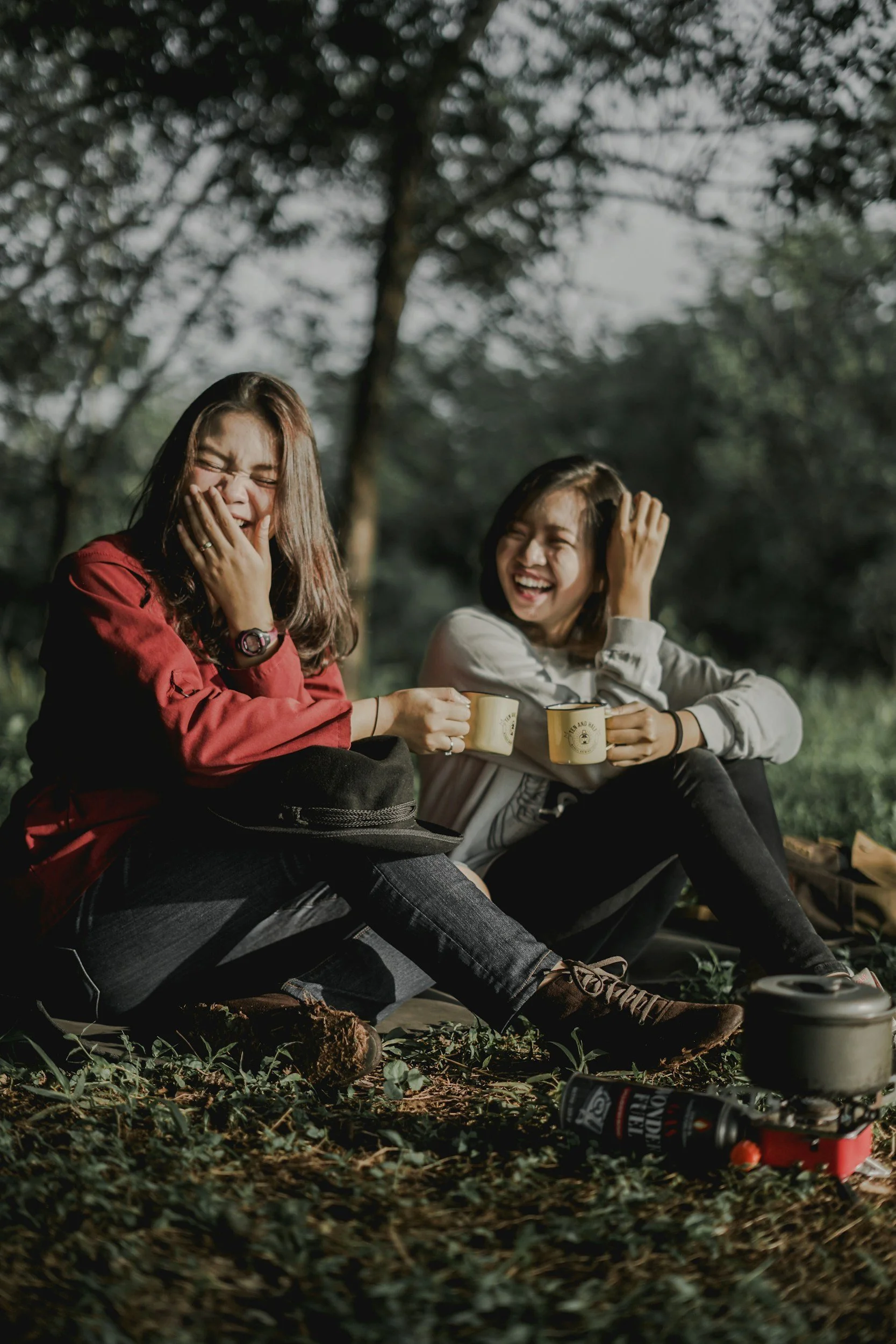 Two friends laughing outdoors while holding mugs during a camping trip