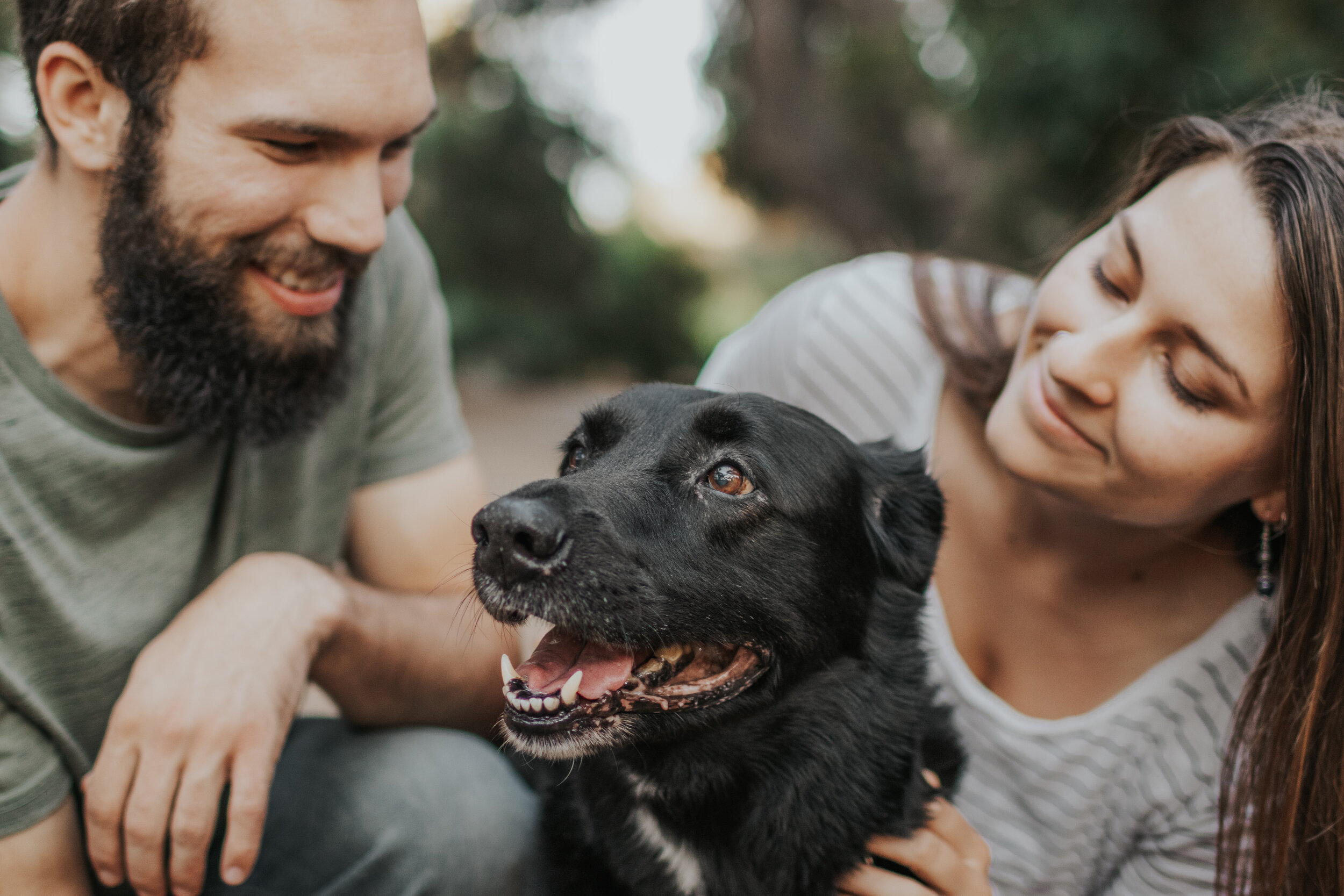 Couple bending down and looking lovingly at their black lab.