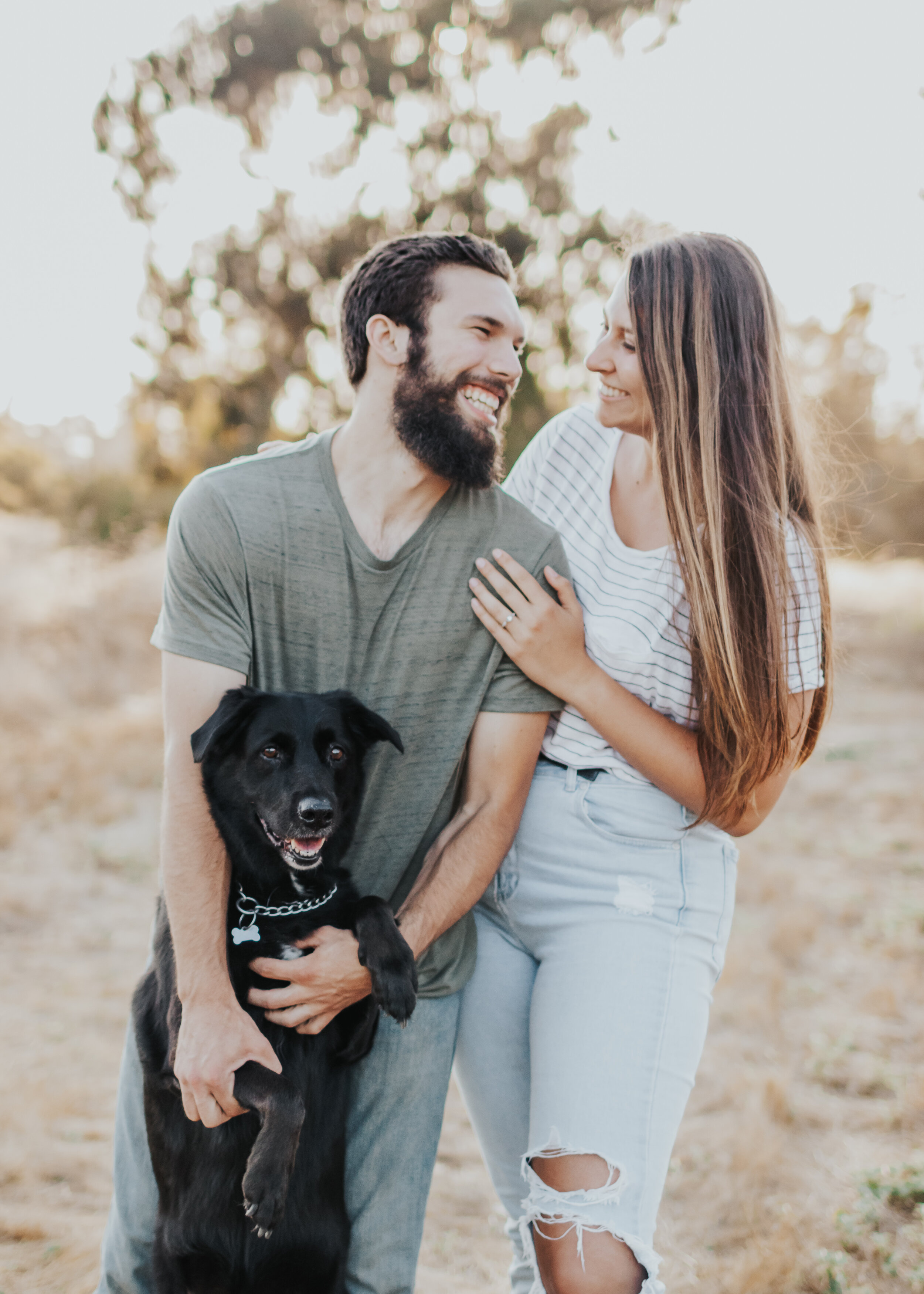 Engaged couple embracing each other and their dog.