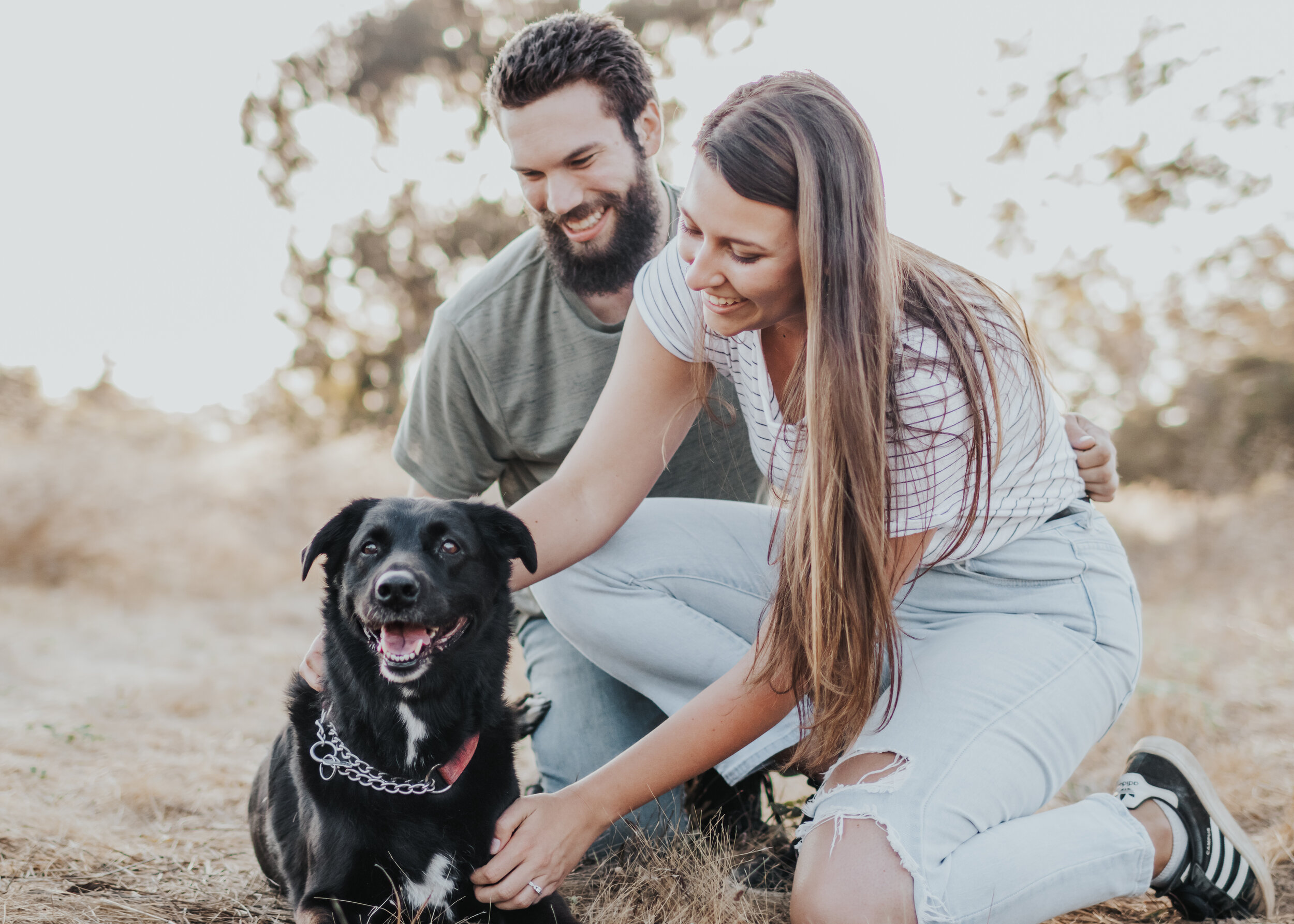 Couple sitting in field with their dog.