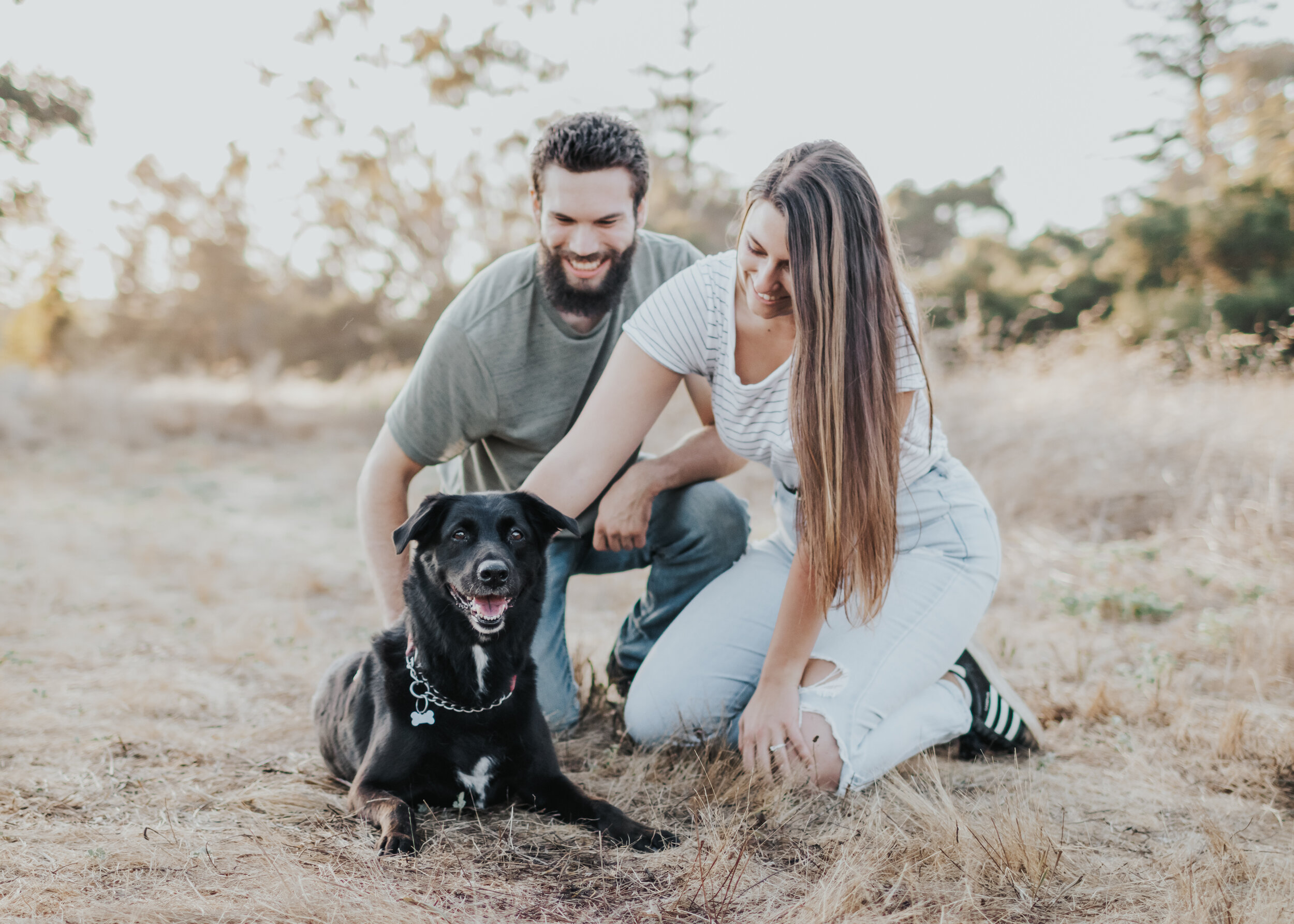 Couple petting their pup in a field.
