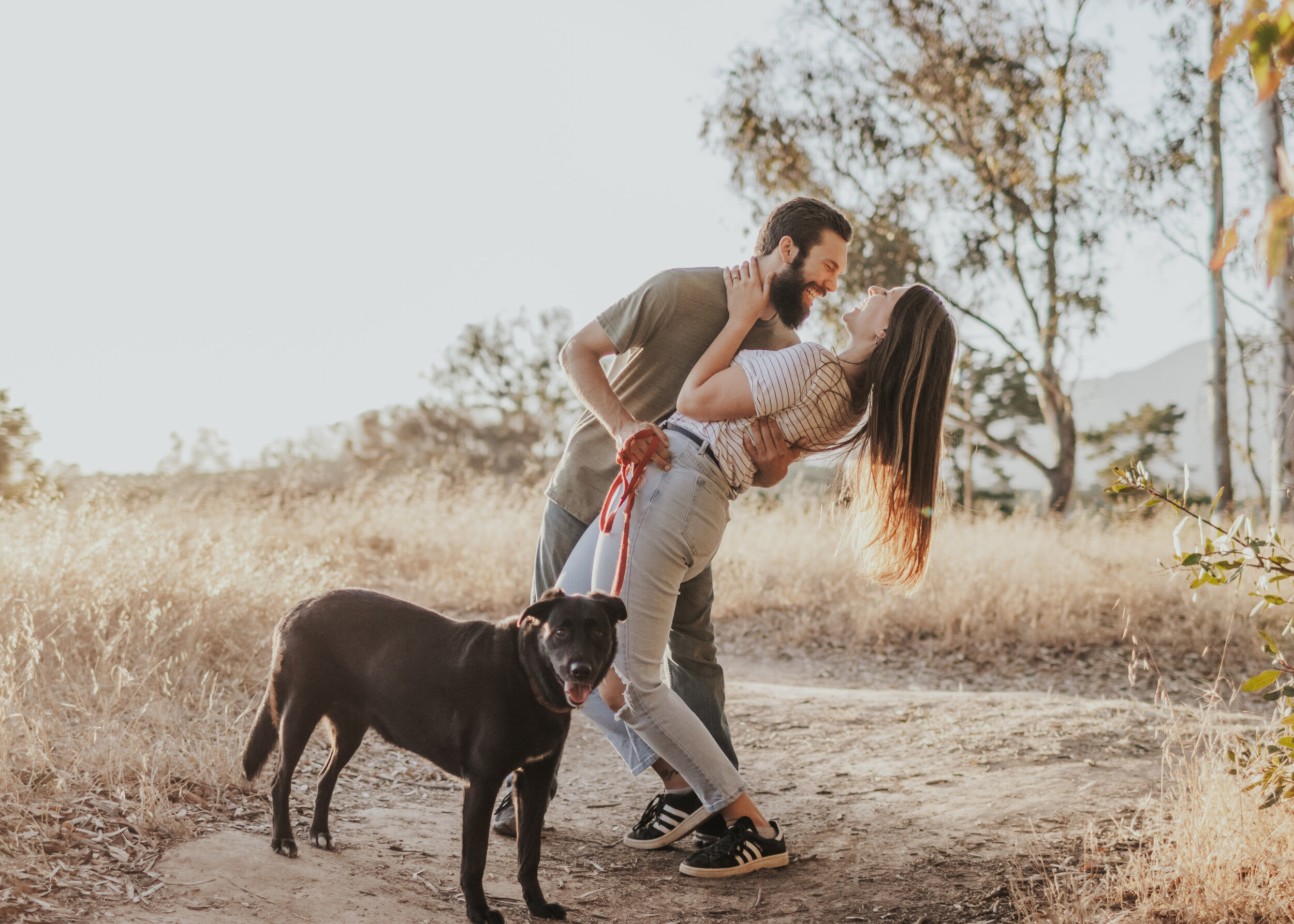 Engaged couple kissing with black lab in foreground.
