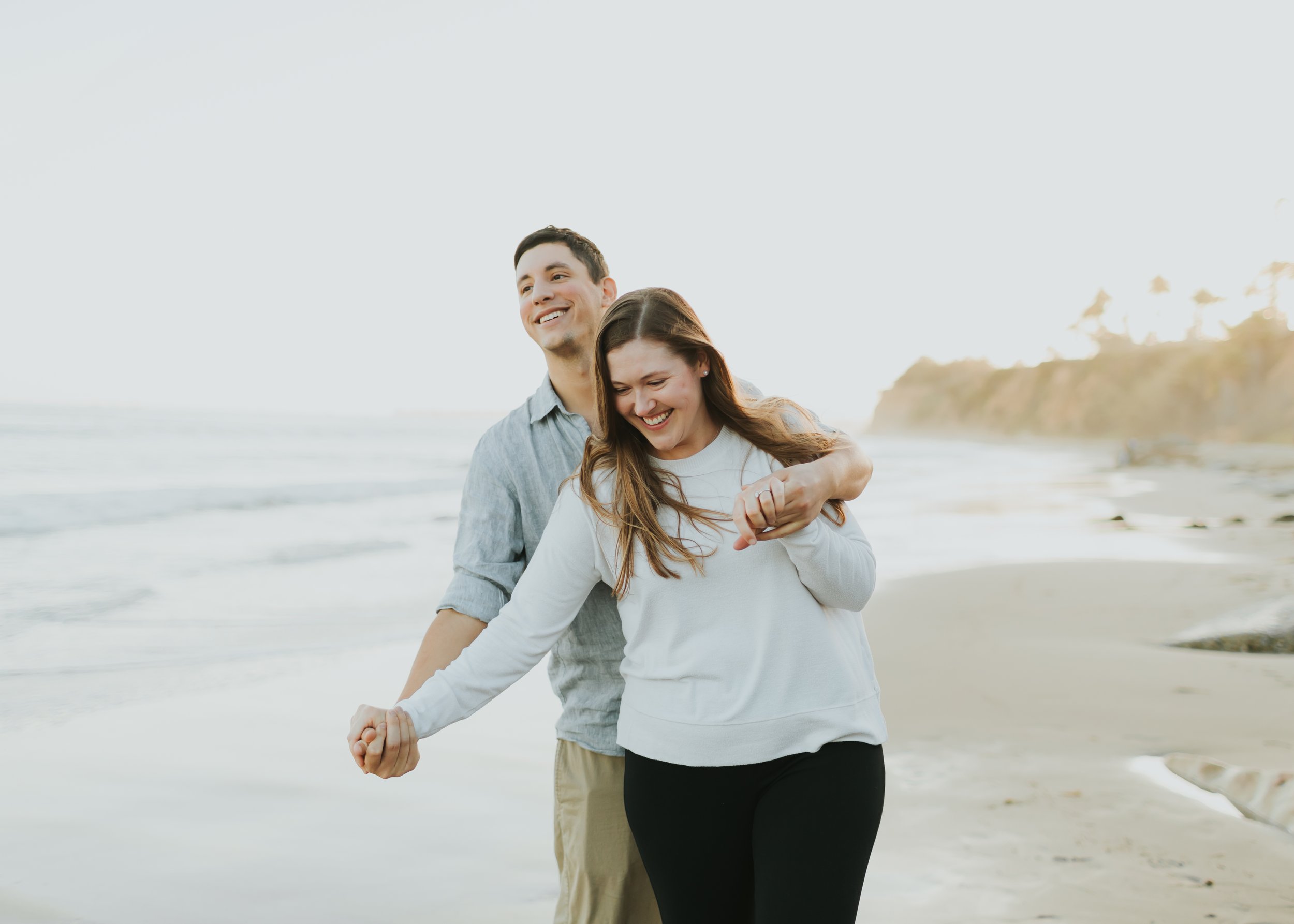 Couple walks forward in goofy embrace during sunset at Butterfly Beach in Santa Barbara.