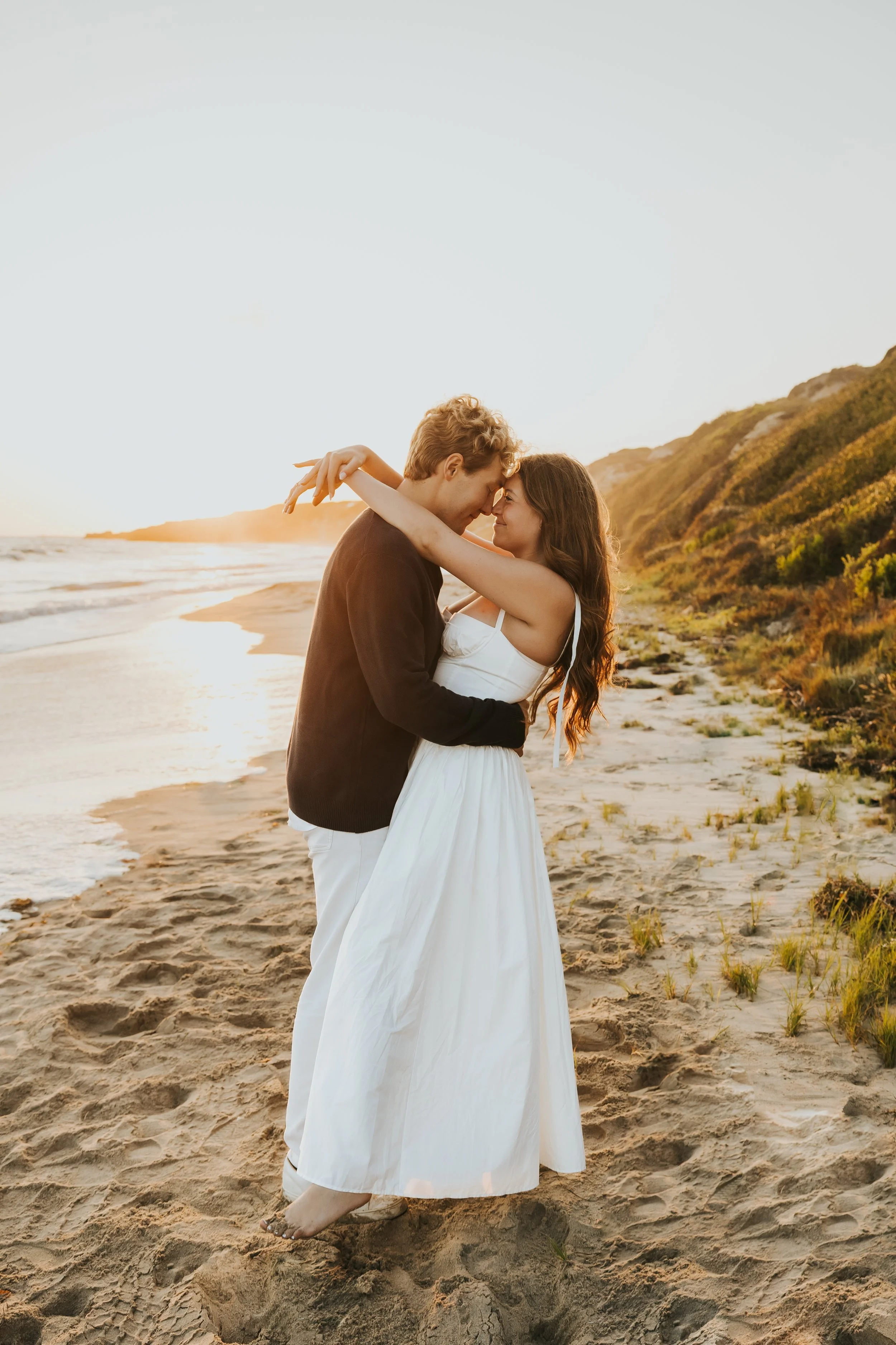 Recently engaged couple wraps their arms around each other on the PNW coastline at sunset.