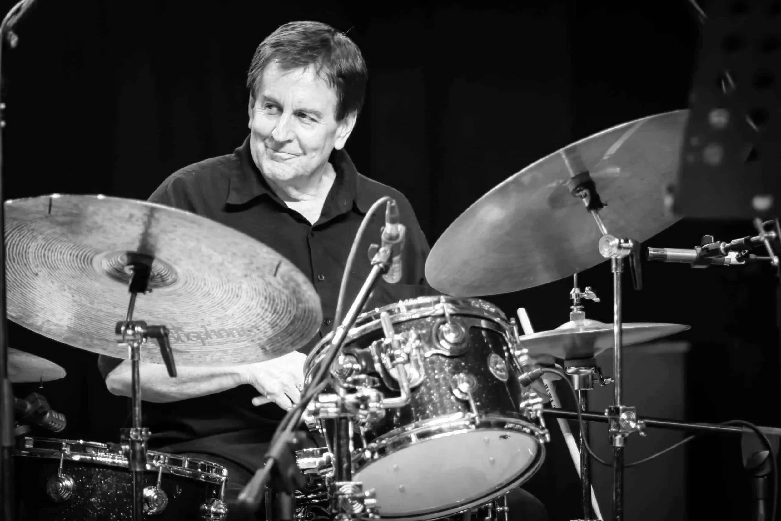 Black and white photo of a drummer playing a drum set with cymbals, focused on the musician.
