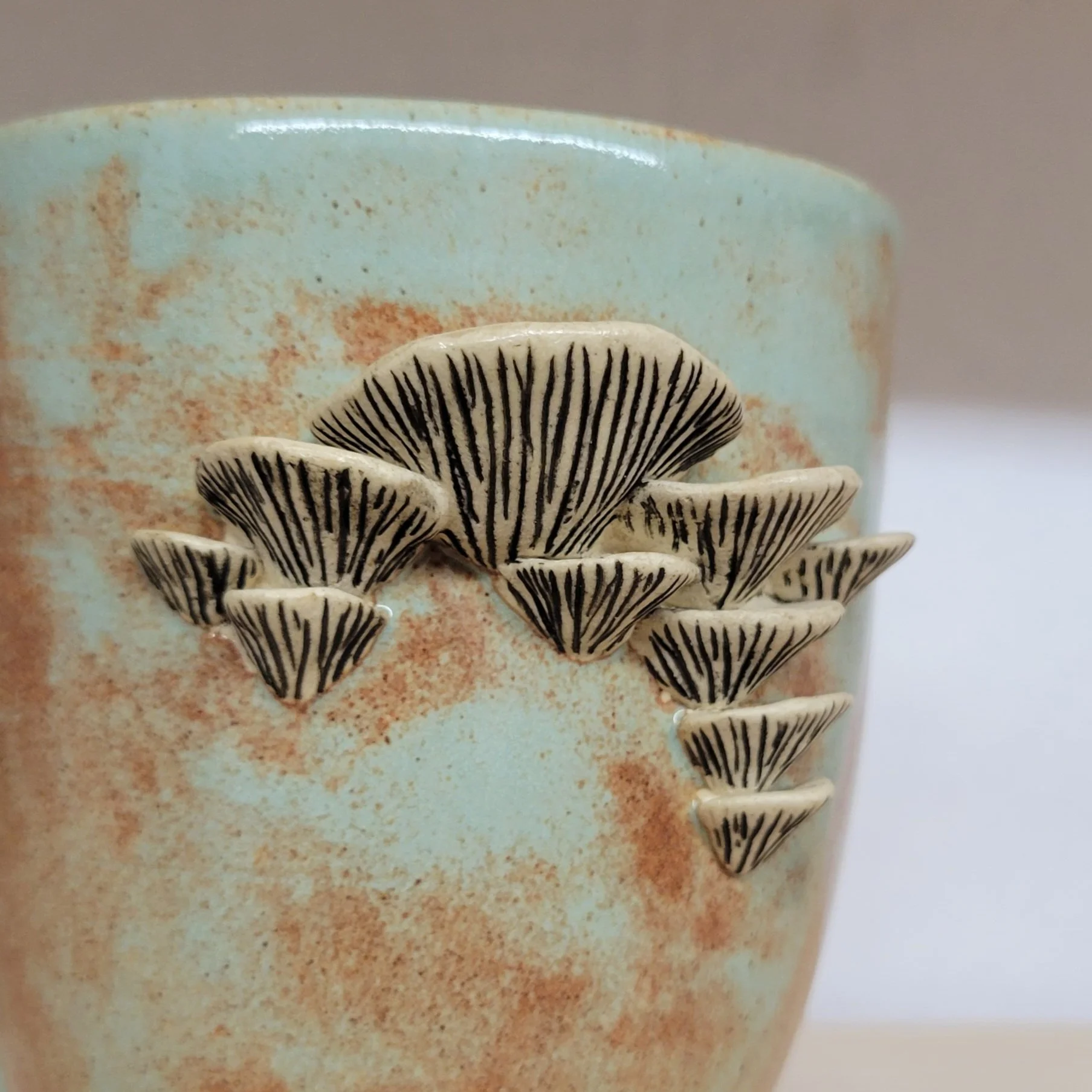 Ceramic cup with beige background and a cluster of black and white mushroom decorations attached to its surface.