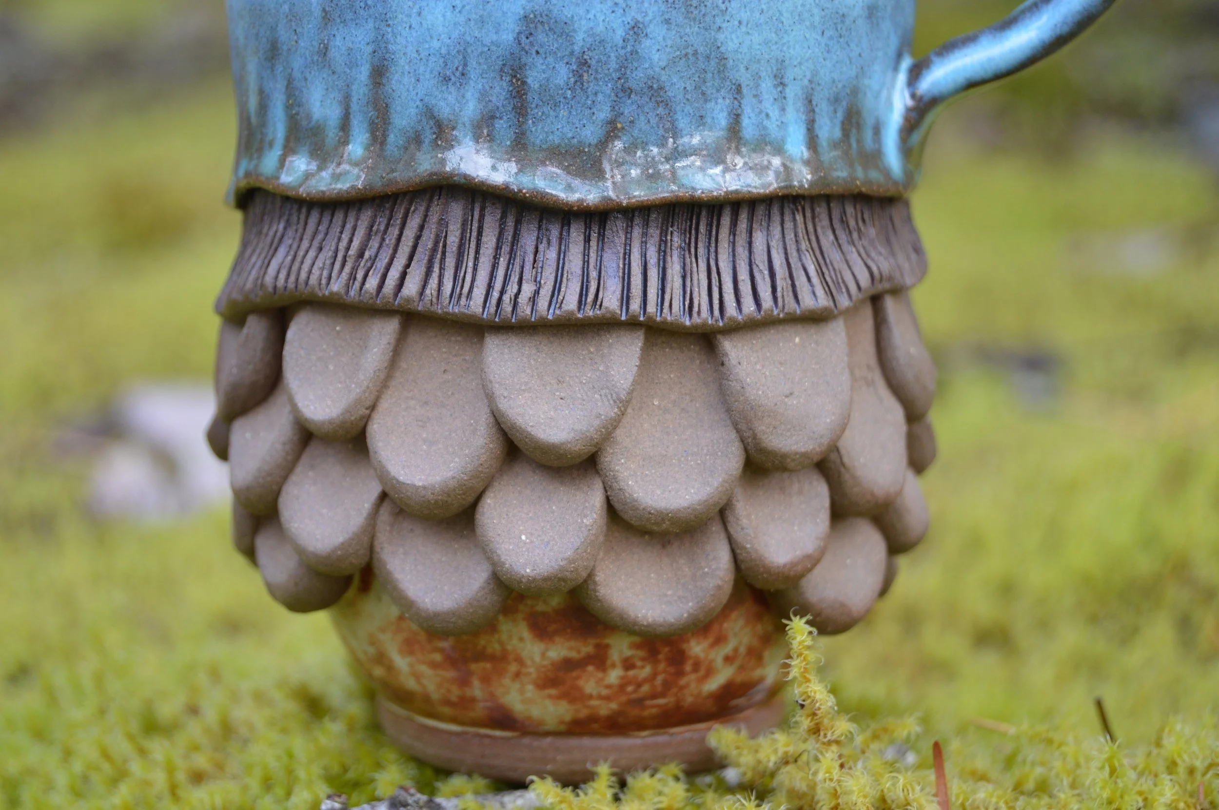 Close-up of a ceramic gnome statue's lower half, showing turban-like topknot, textured beard, and a rounded base, placed on mossy ground.