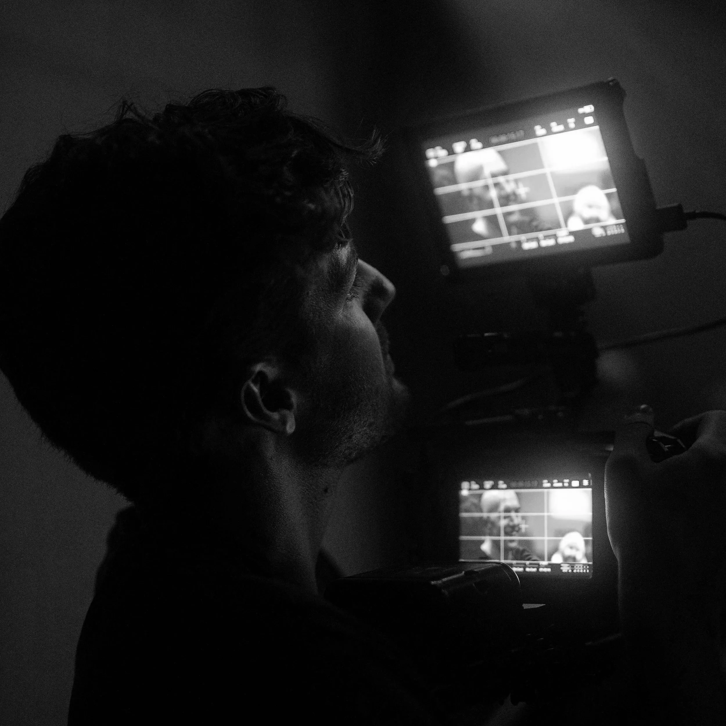 A person operating a camera with two screens, capturing an image in a dark setting.