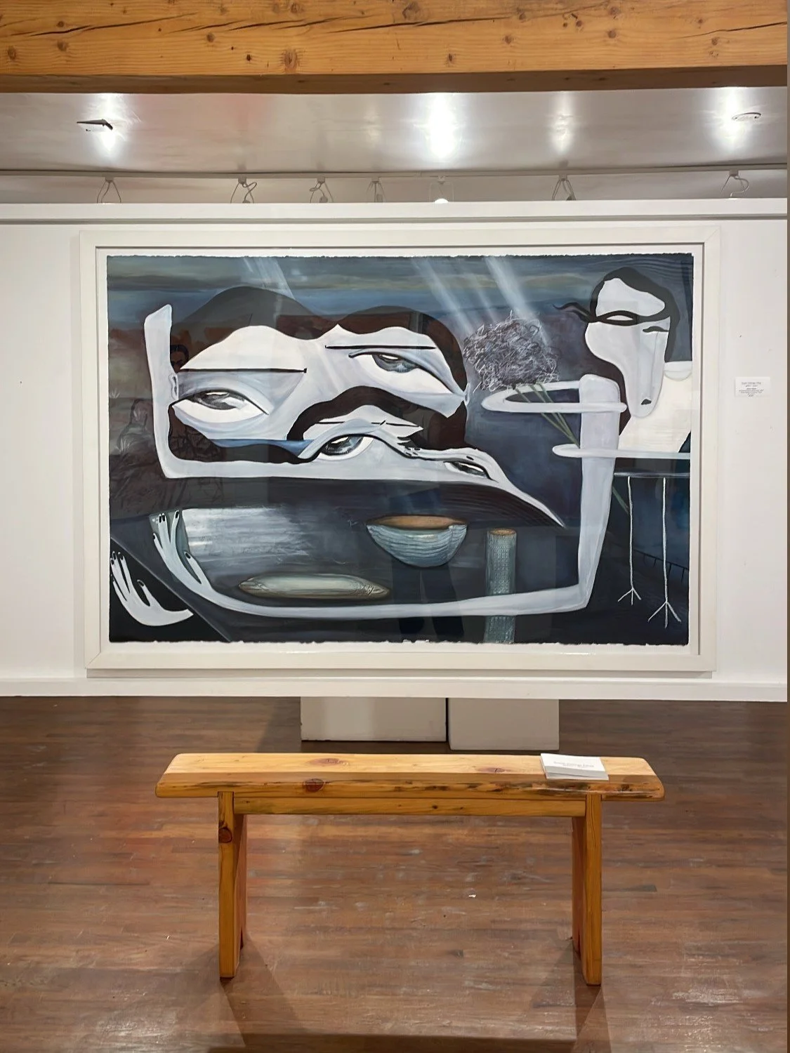 Abstract painting featuring multiple distorted faces with elongated features, muted colors, and surreal elements, displayed in an art gallery.