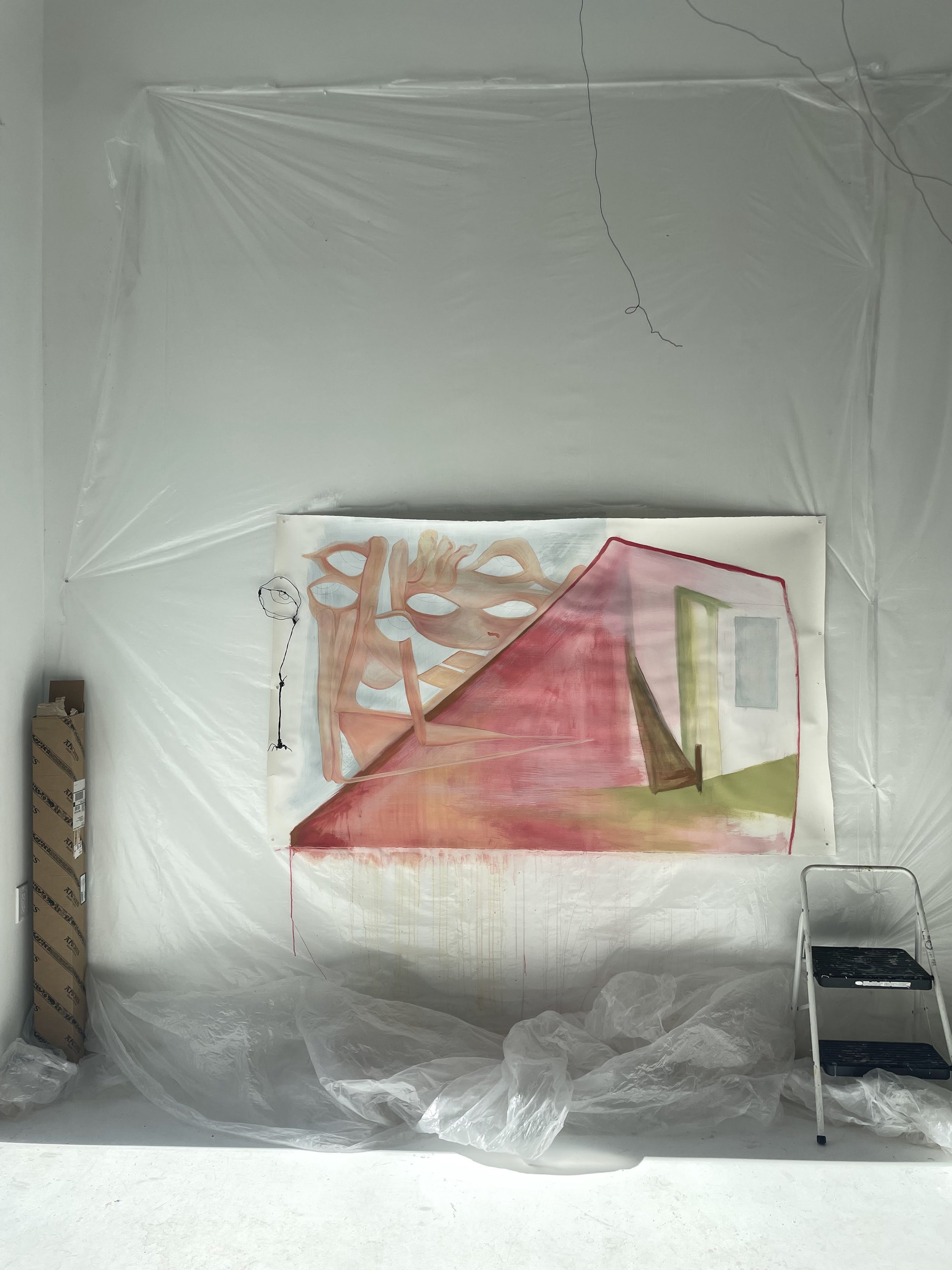An art studio or workshop with plastic sheeting on the walls and ceiling. There is a large abstract painting featuring a stylized anatomical heart and a house with a chimney painted on a large canvas. The floor is covered with plastic, and there are 