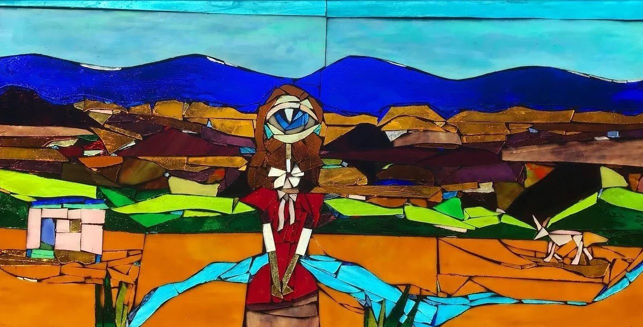 A stained glass art piece depicting a woman with an eye for a face, standing outdoors in a landscape with mountains, fields, and a small house.