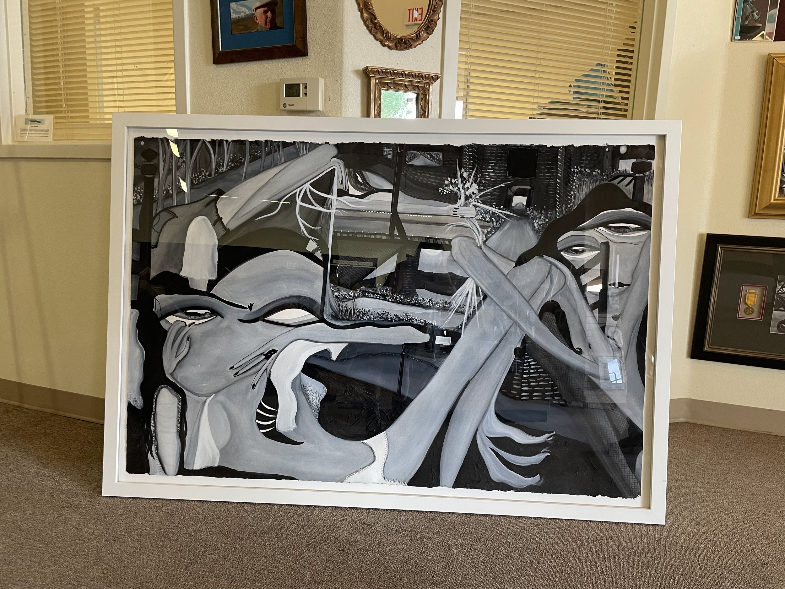 Black and white painting of a woman with long hair, wearing a bra, with her hands placed on her head. The artwork is framed and displayed indoors.