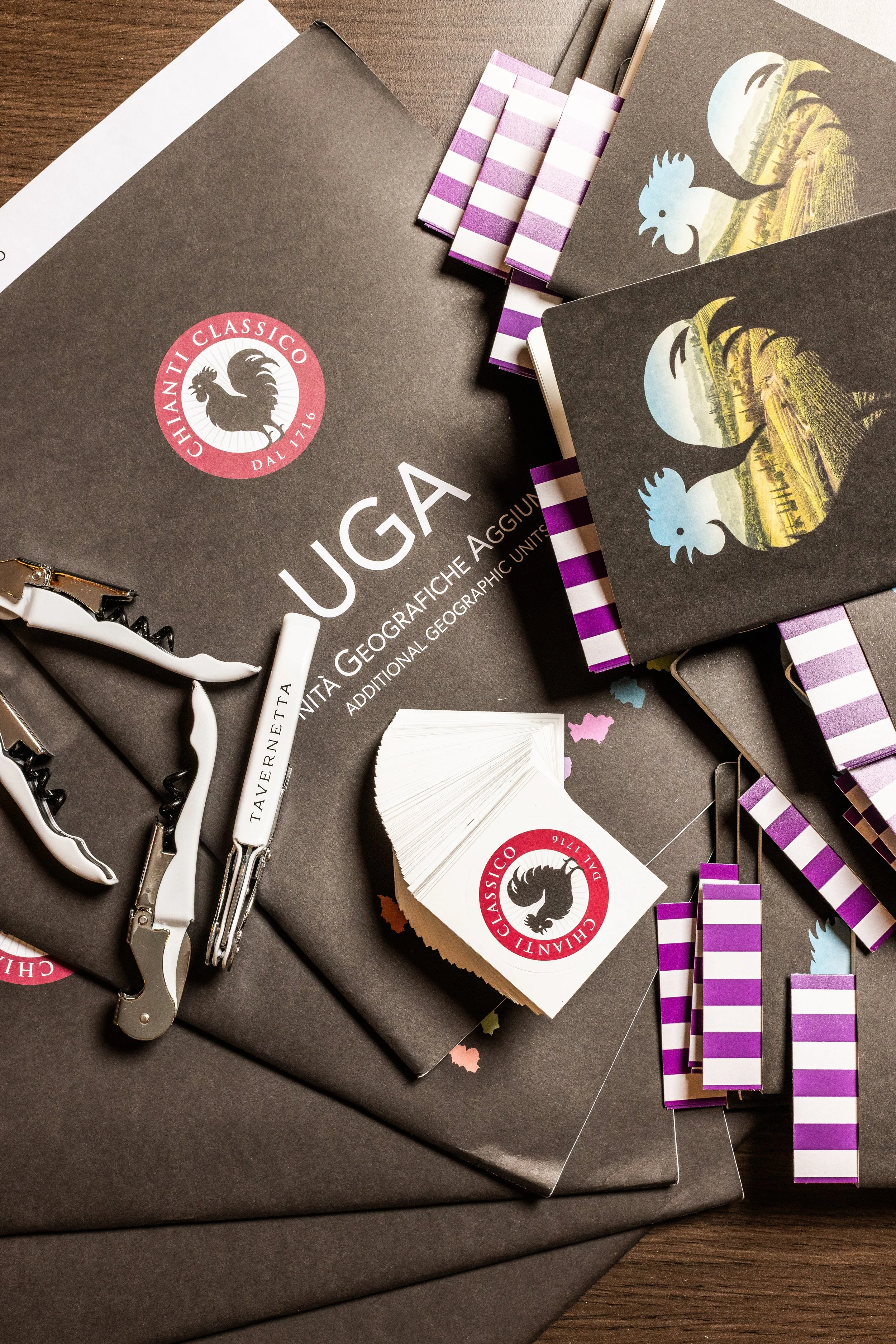 Workshop or event supplies for Chianti Classico with folders, business cards, pens, and decorative stickers, on a wooden surface.