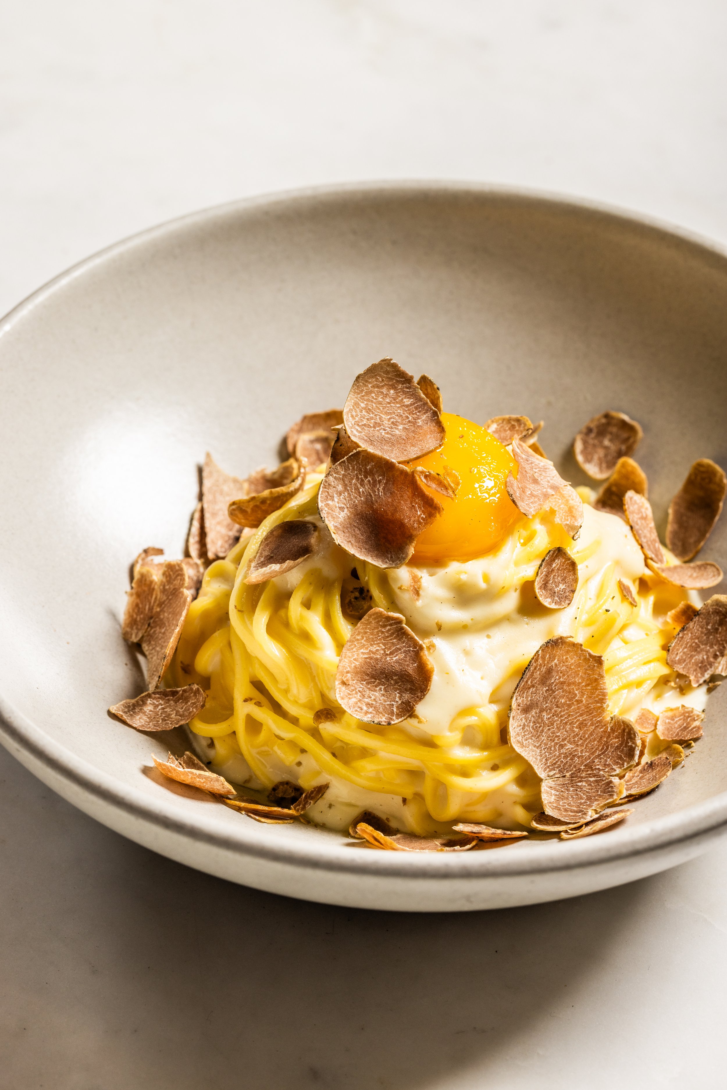 A bowl of spaghetti topped with a poached egg, shaved truffles, and creamy sauce.