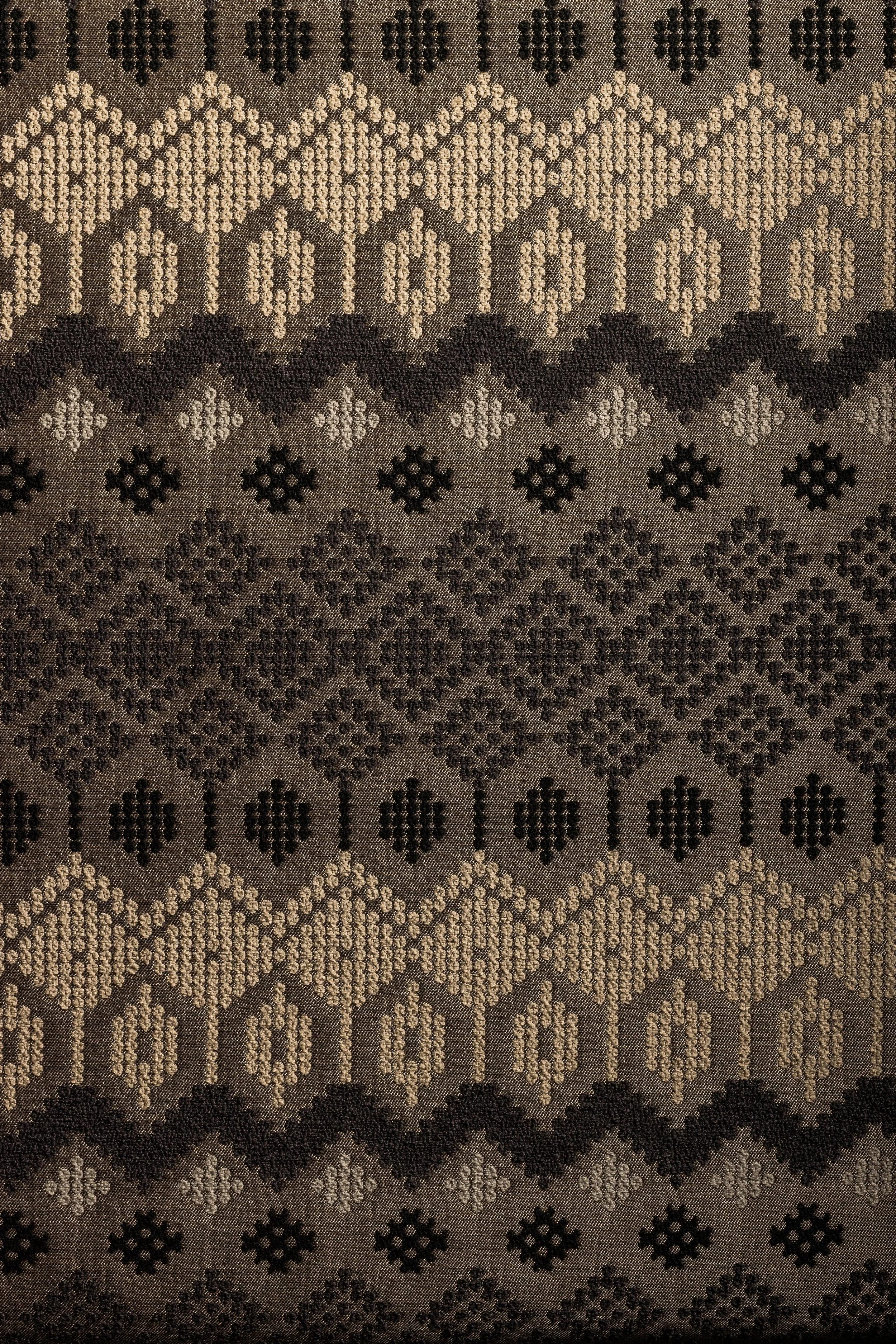 A patterned textile fabric with black and beige geometric designs, including diamonds, zigzags, and small floral motifs.