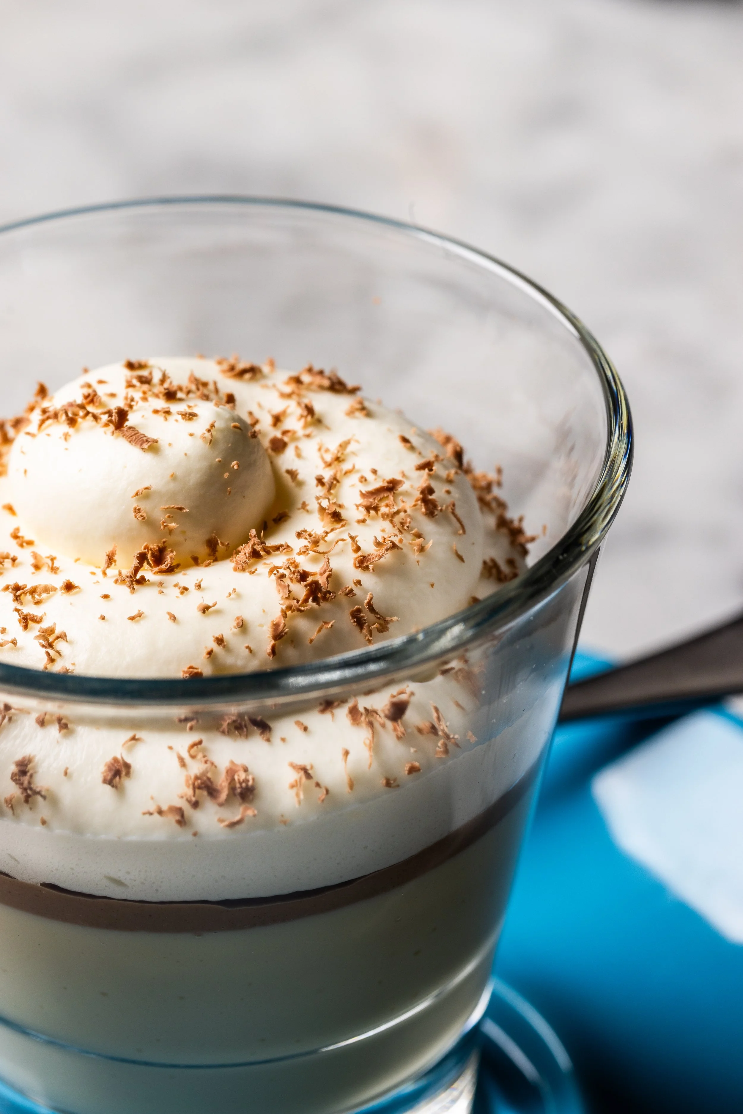 A glass dessert cup filled with layered tiramisu, topped with whipped cream and chocolate shavings.