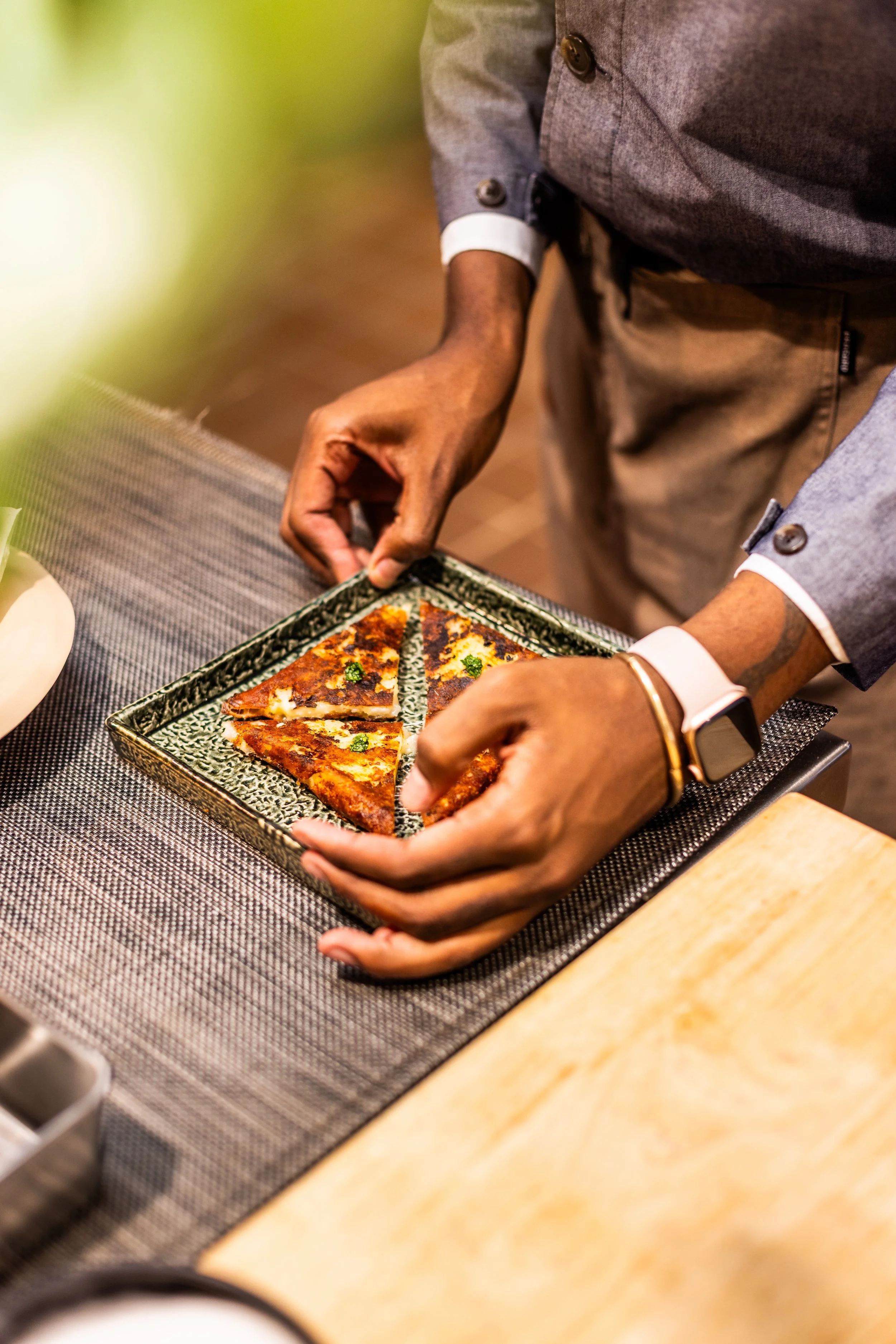Person placing slices of pepperoni pizza on a green patterned plate.