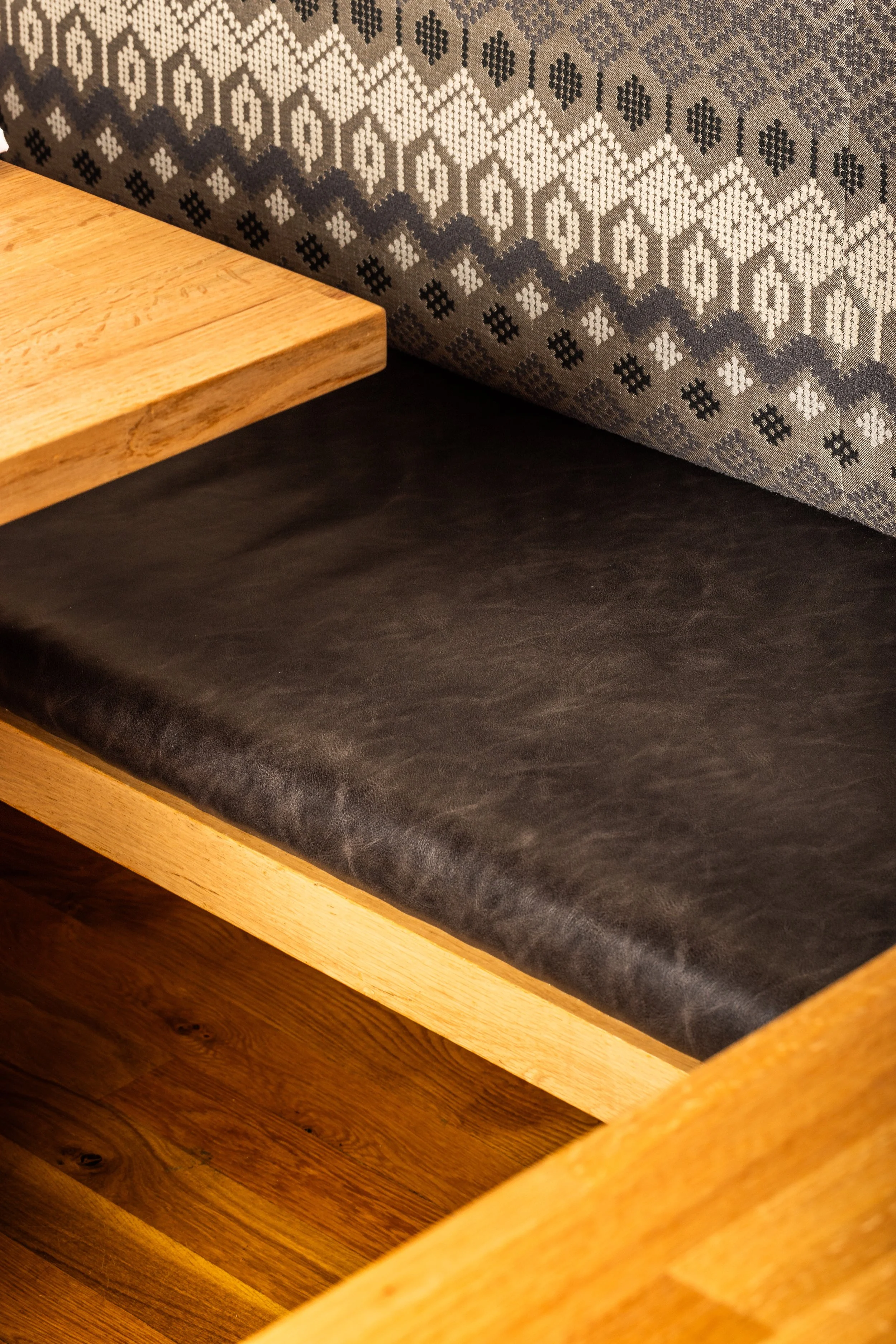 Close-up of a wooden bench with a black leather cushion and a patterned fabric backrest.