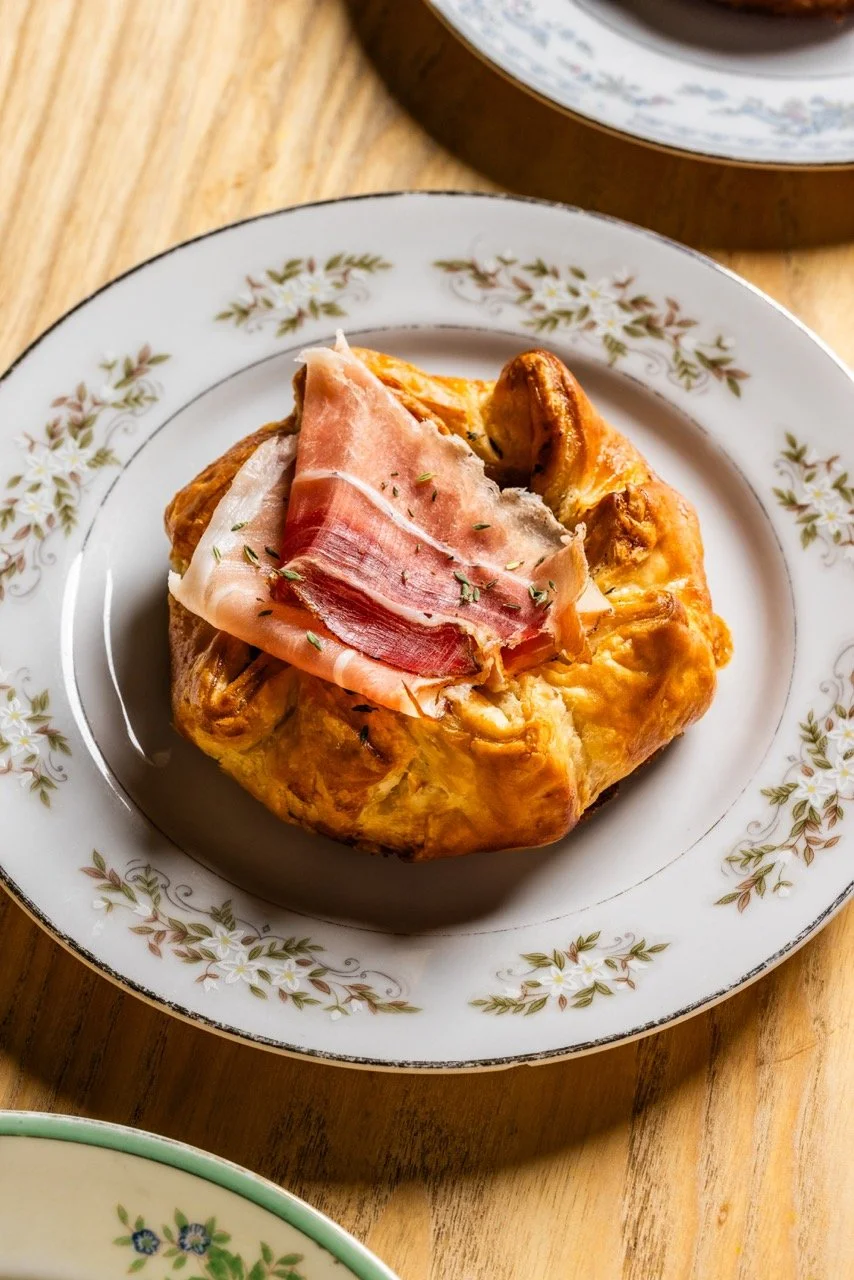 A savory breakfast casserole topped with a slice of ham, served on a floral-patterned plate.