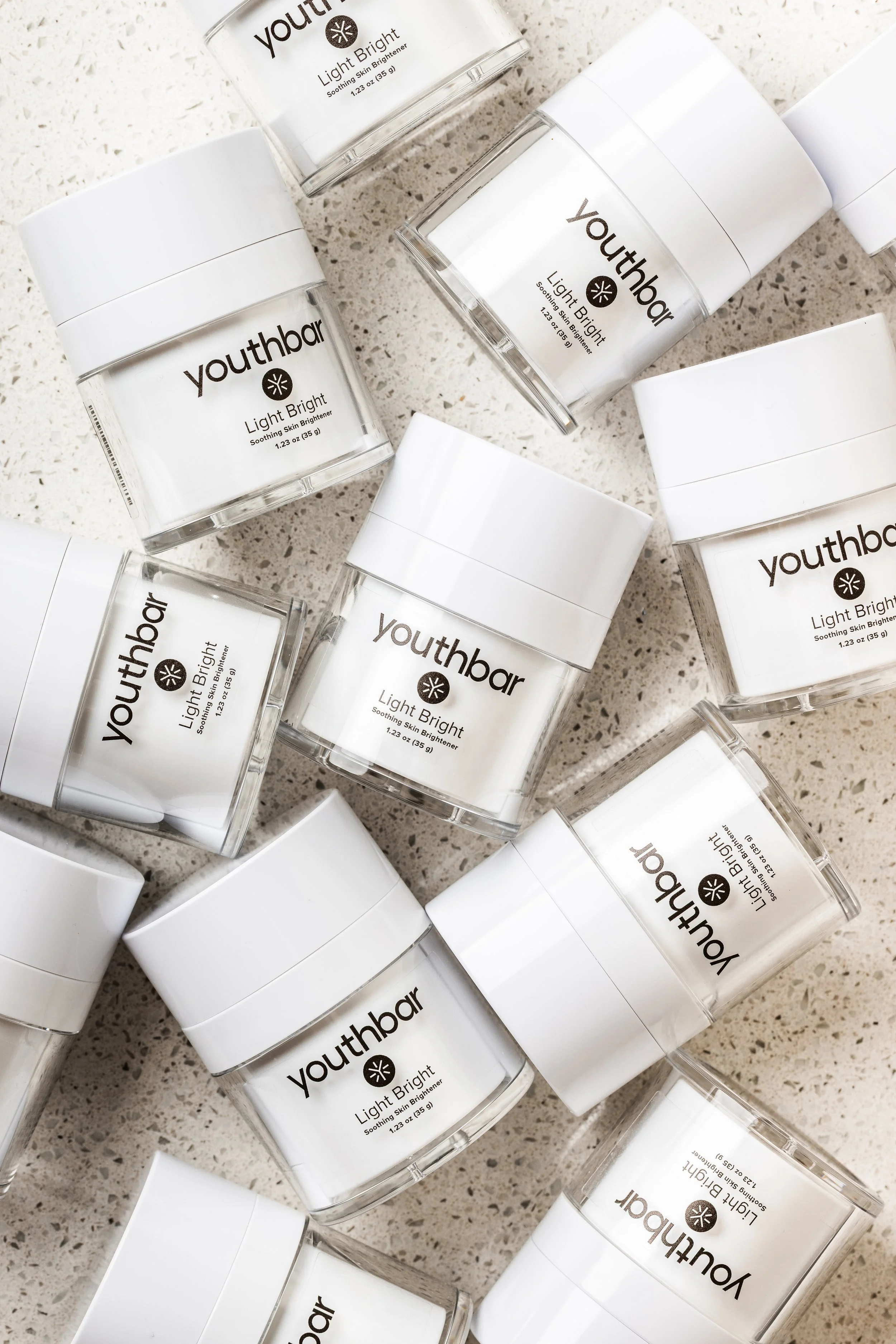 Multiple jars of Youthbar Light Bright soothing skin brightener arranged on a speckled surface.