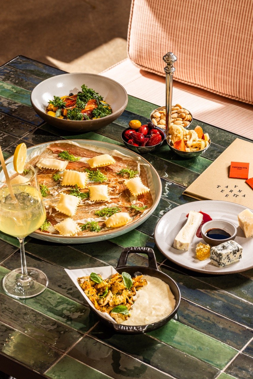 A table set with cheese, charcuterie, fresh vegetables, cherries, nuts, wine, and a salad.