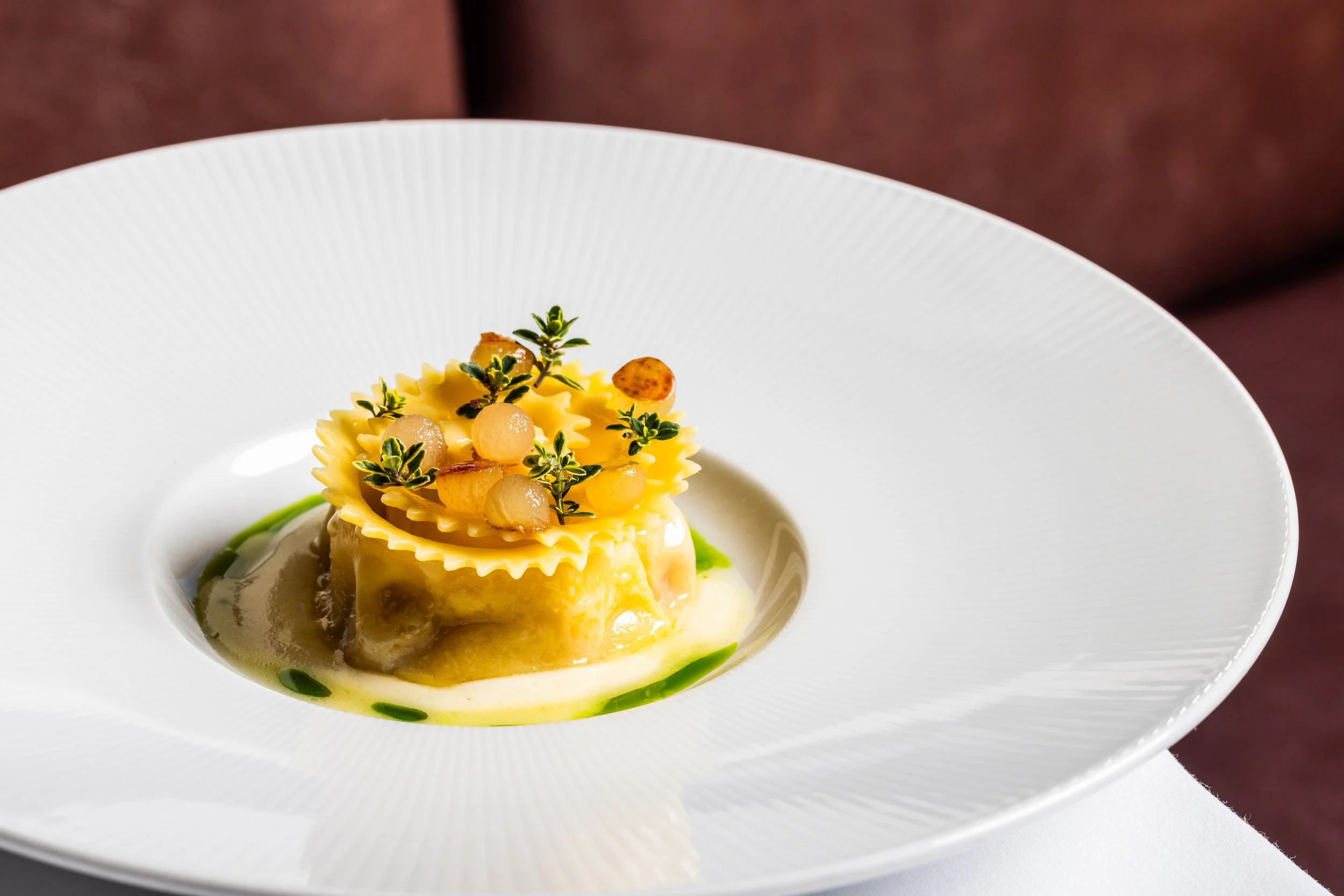 Elegant plated dish featuring pasta topped with small garnished herbs and pearl onions, served on a white plate.