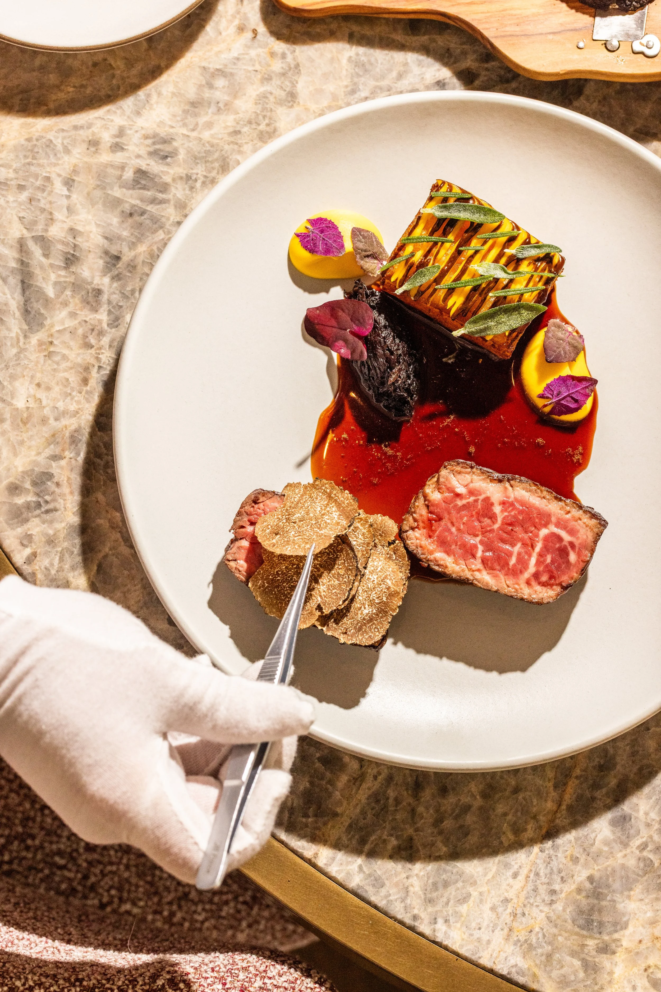A plated high-end beef dish with various garnishes and sauces on a white round plate.