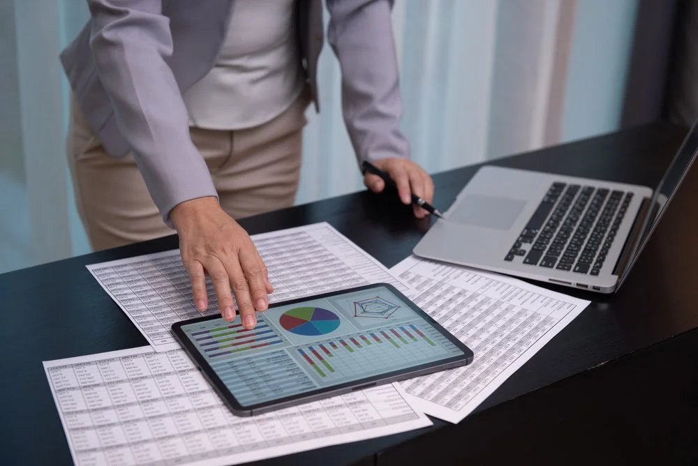 Stock photo of person reviewing budget documents on paper, tablet and computer