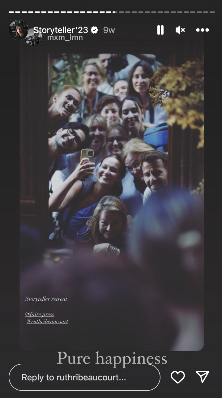 Group of women and one man taking a selfie together, smiling and enjoying themselves at a retreat. The setting appears cozy and indoor, with a wooden frame and yellow flowers visible in the background.