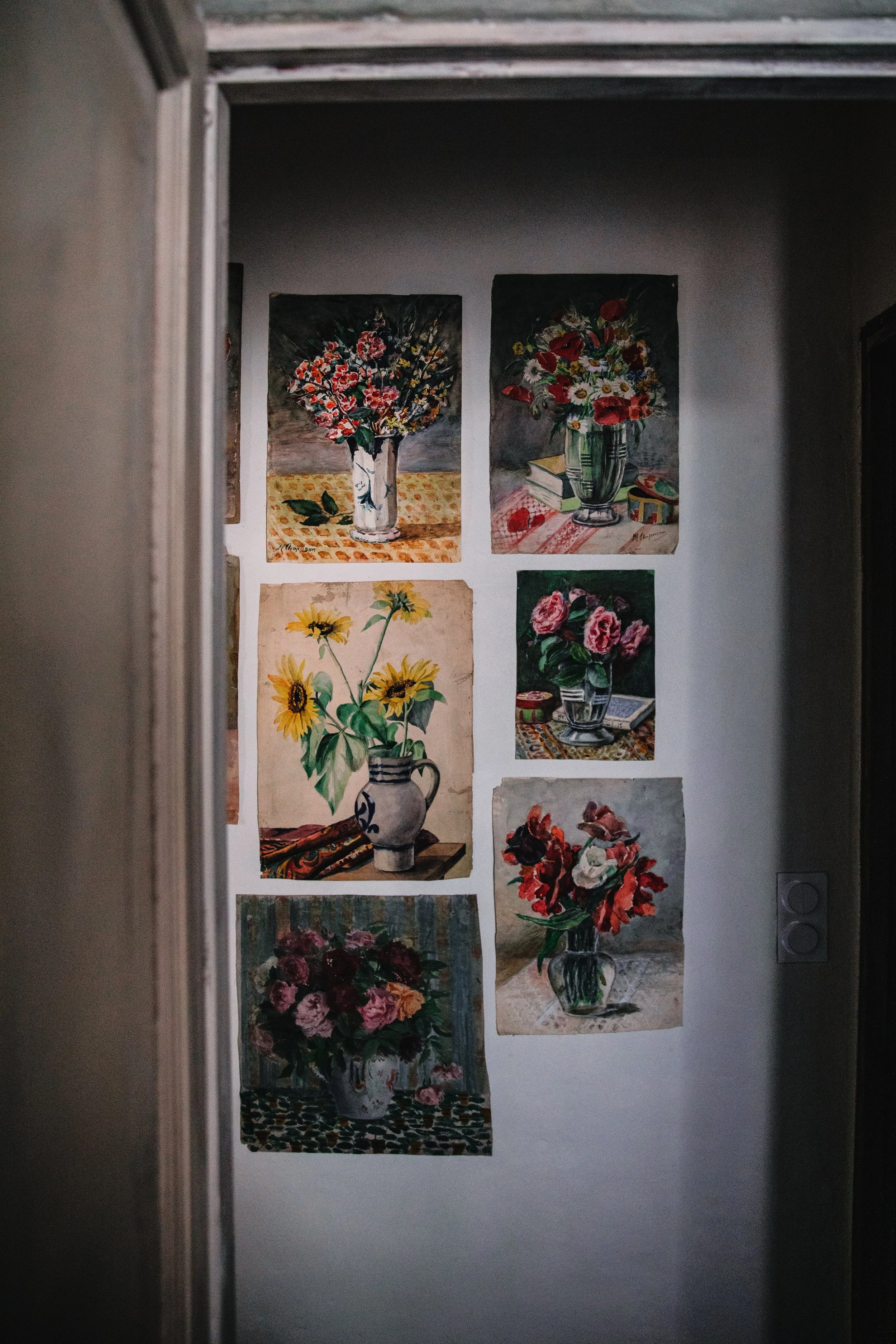 Gallery wall displaying seven still life paintings of various flower arrangements in vases.