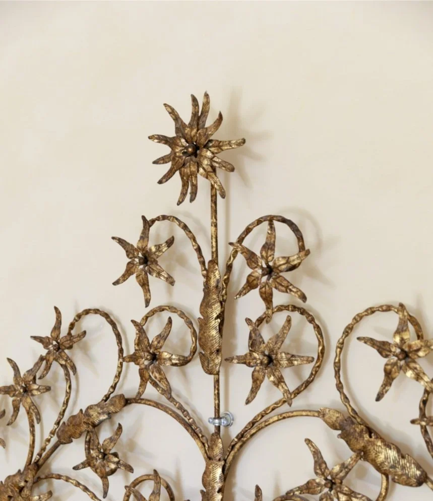 Close-up of an ornate gold-colored metal wall decoration with flowers and leaves.