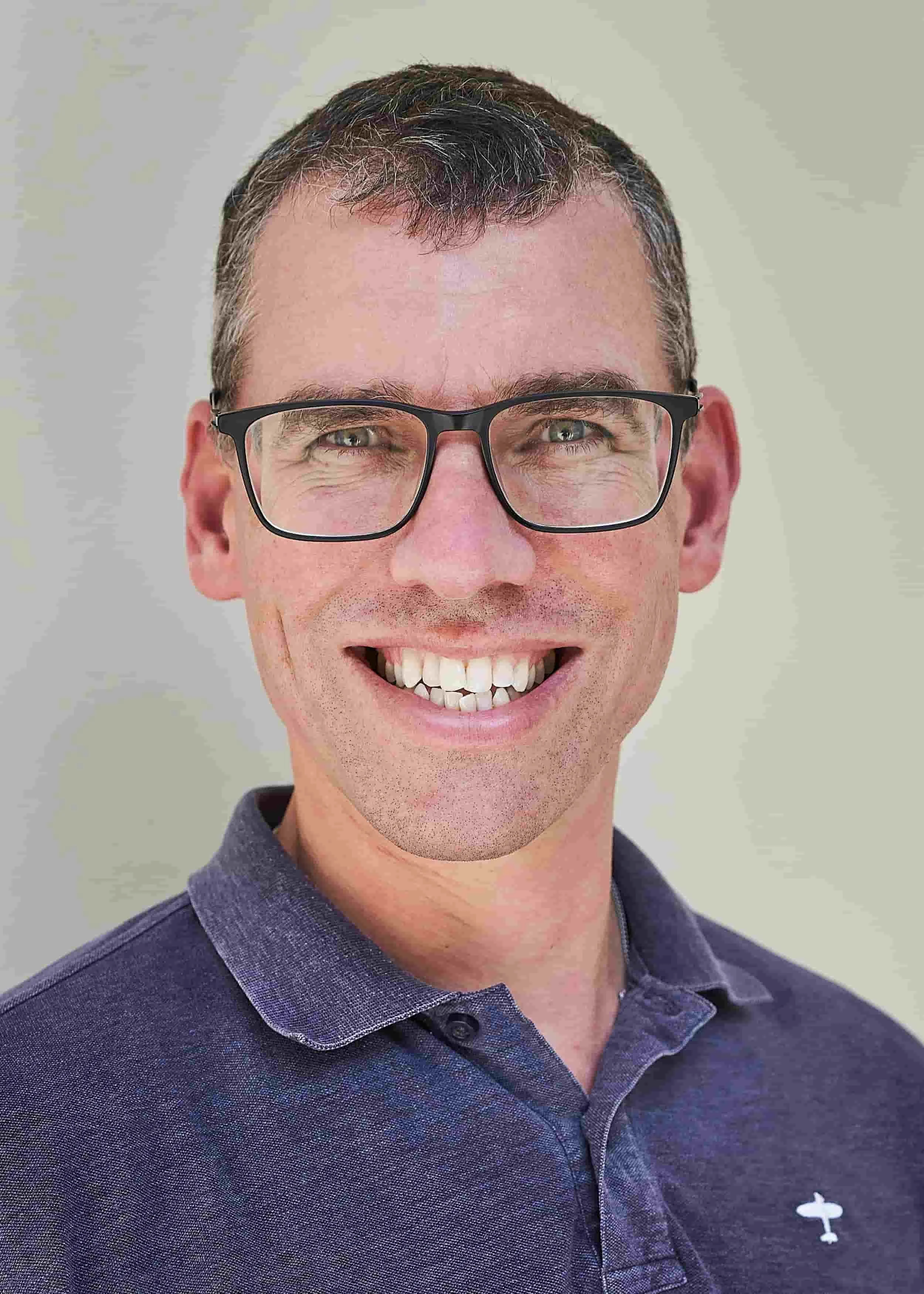 Photo of Simon Chapman smiling, wearing glasses and a polo shirt.