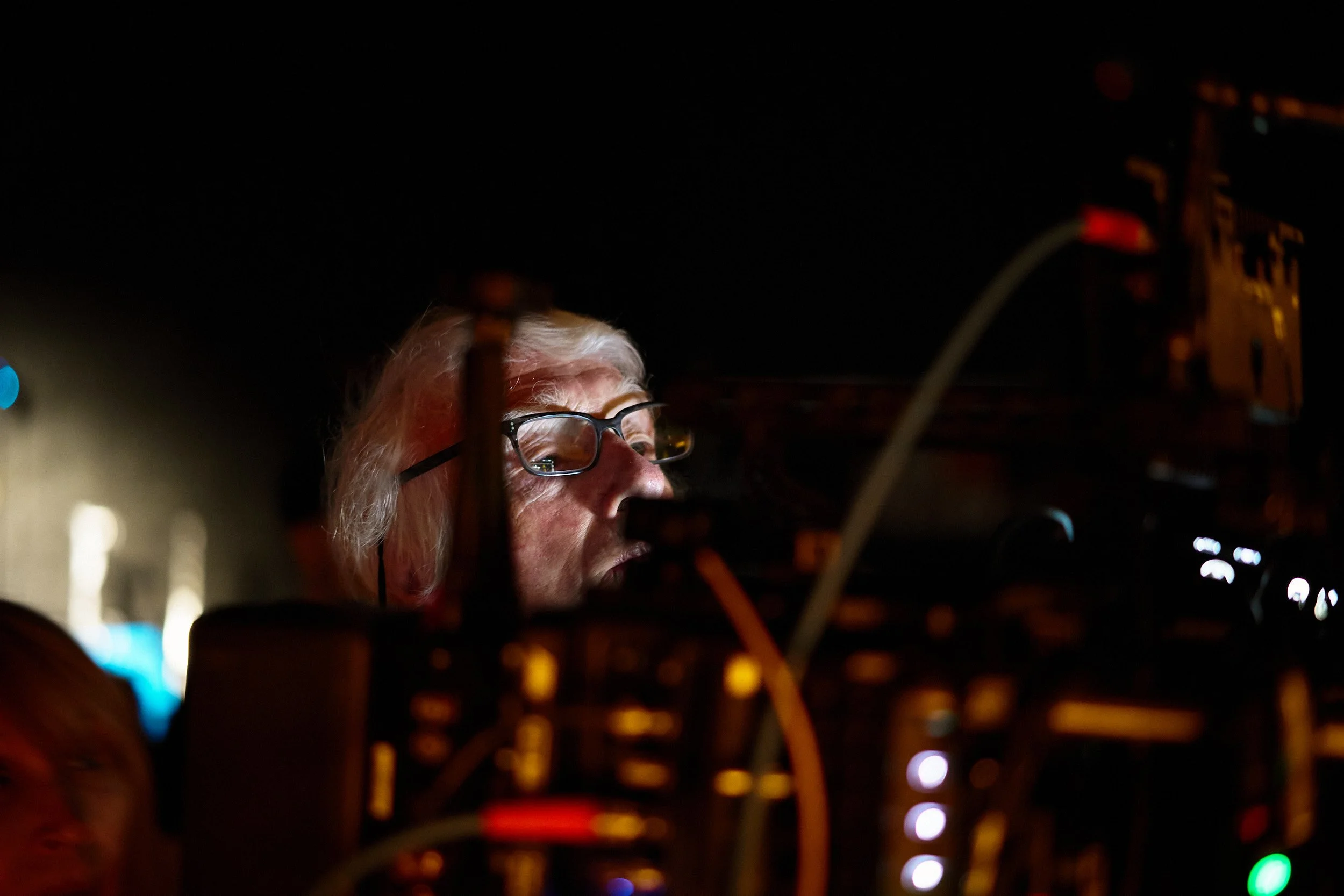 Close-up of an elderly person with white hair and glasses working with electronic equipment at night.