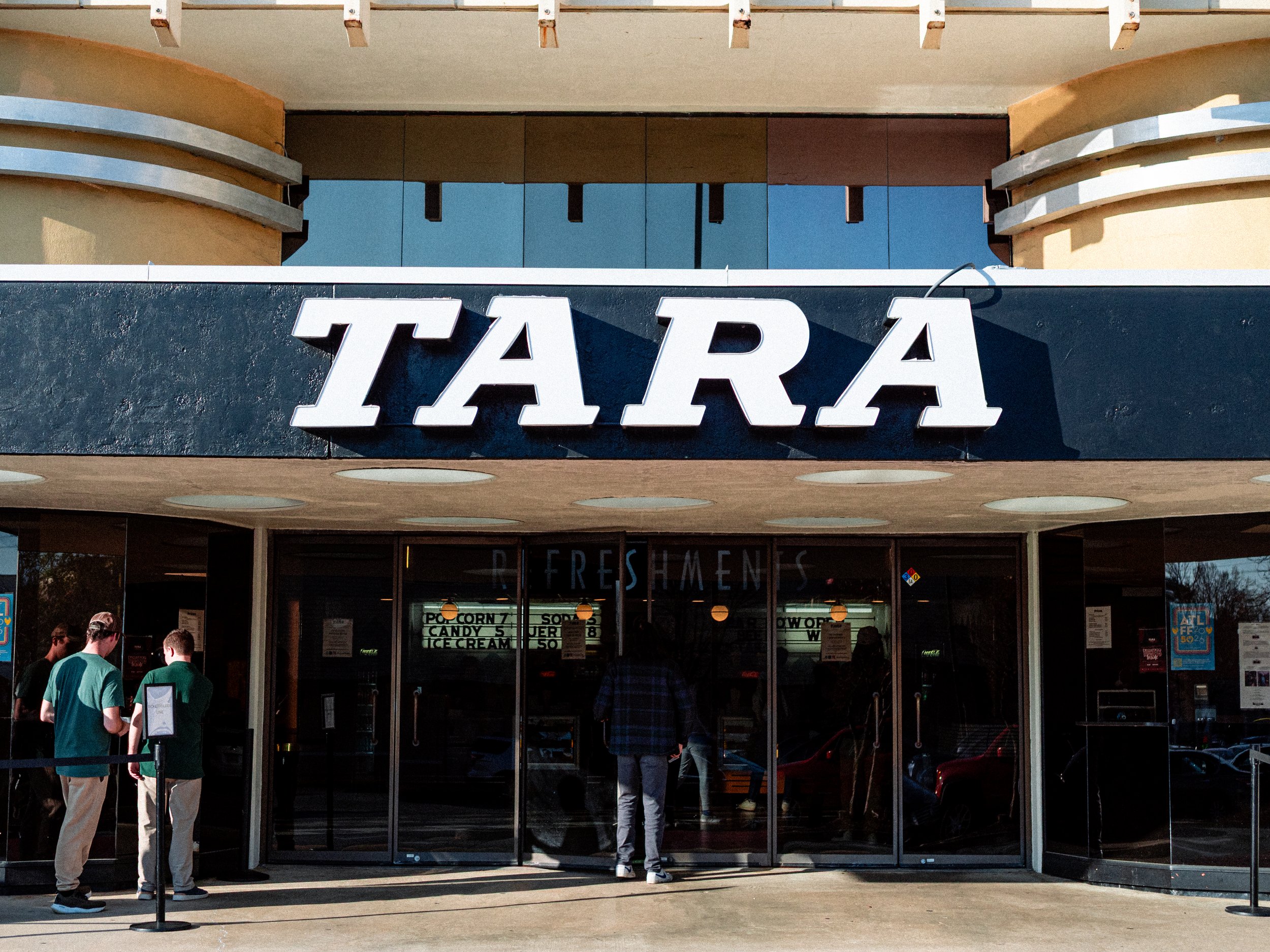 People standing in line outside a food stand with a sign that says 'TARA.'