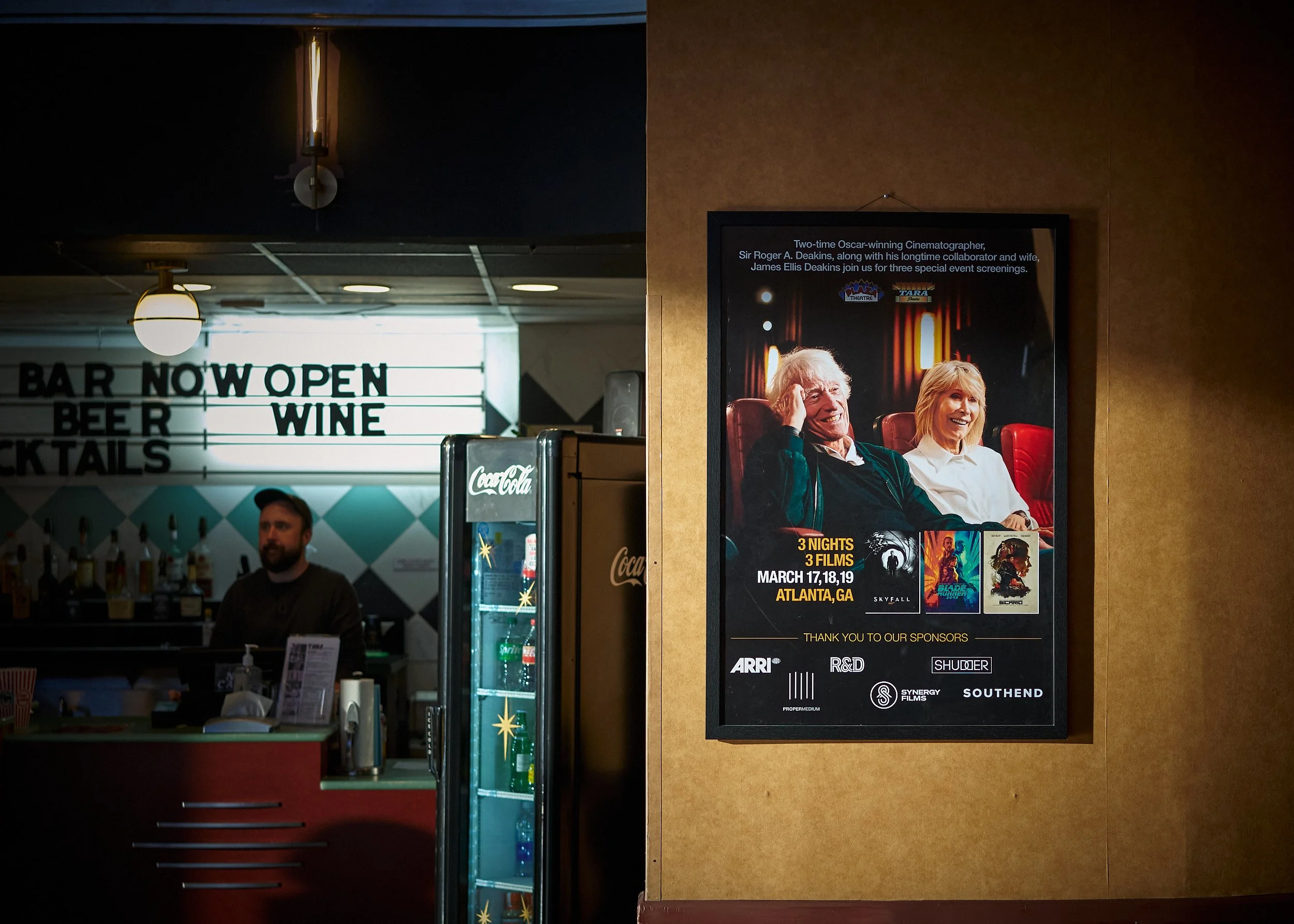 A movie poster on a wall advertising a film screening event in Atlanta, Georgia, from March 17 to 19. The poster features images of two elderly people, a man and a woman, smiling and sitting together. The background of the poster includes a theater s