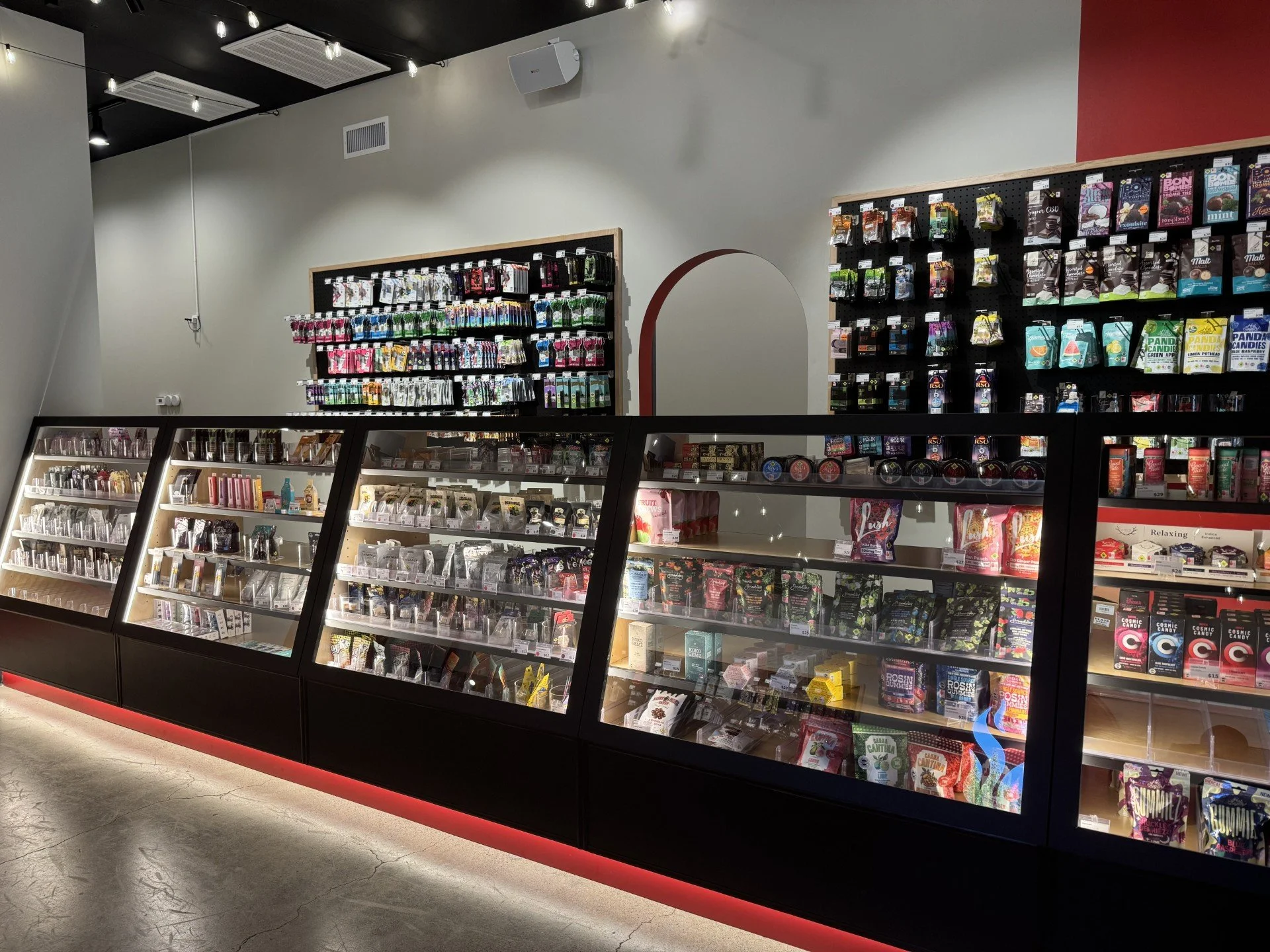 Display case filled with assorted candies and chocolates in a retail store, with shelves of snack packets on the wall in the background.