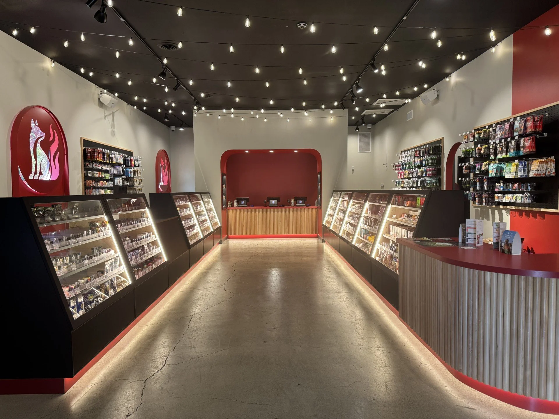 Inside a modern retail store with display cases filled with products, string lights hanging from a black ceiling, and a red and beige color scheme.