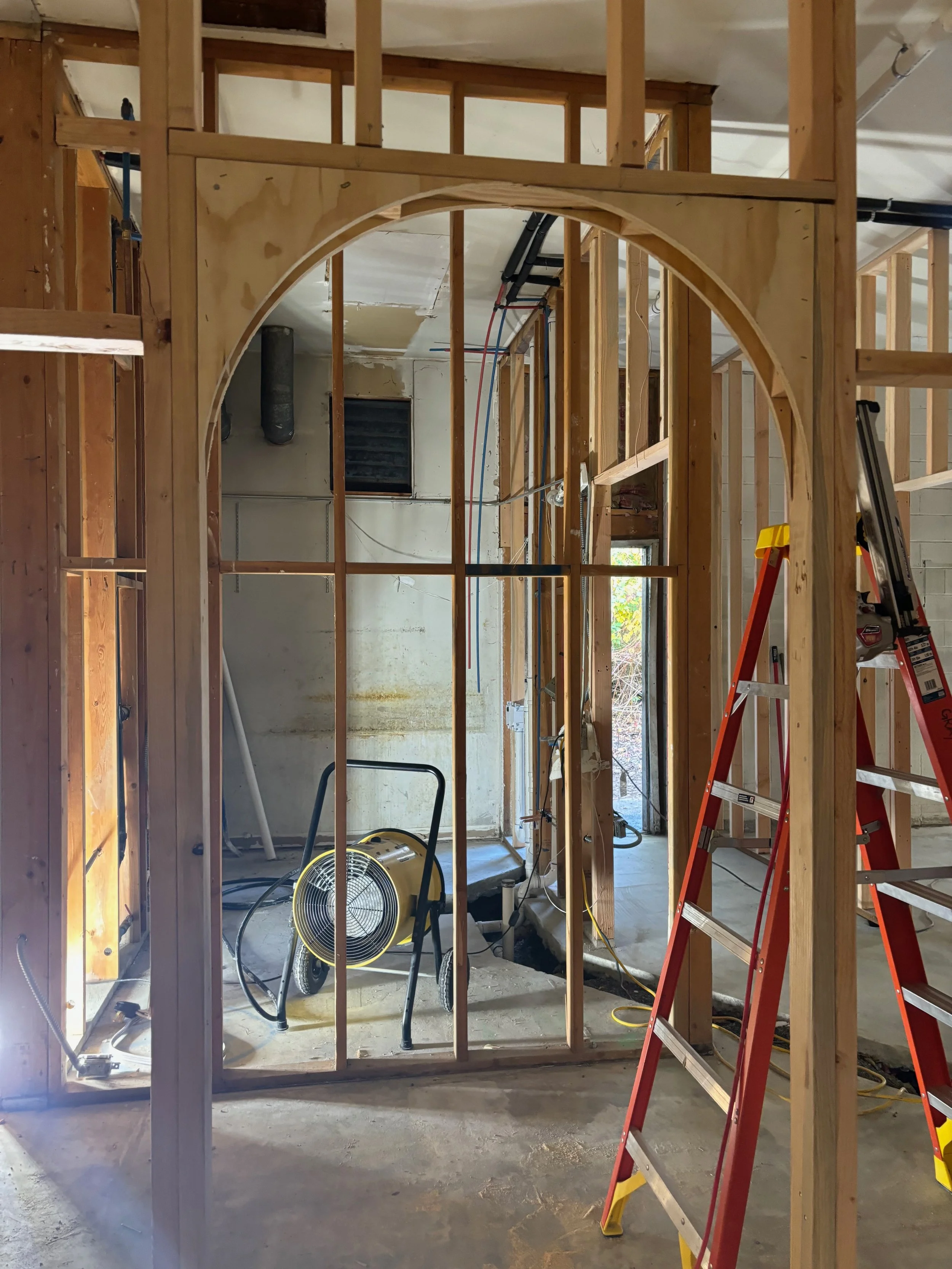 Construction site with wooden framing for a wall and an archway, ladder, and construction tools in the space.