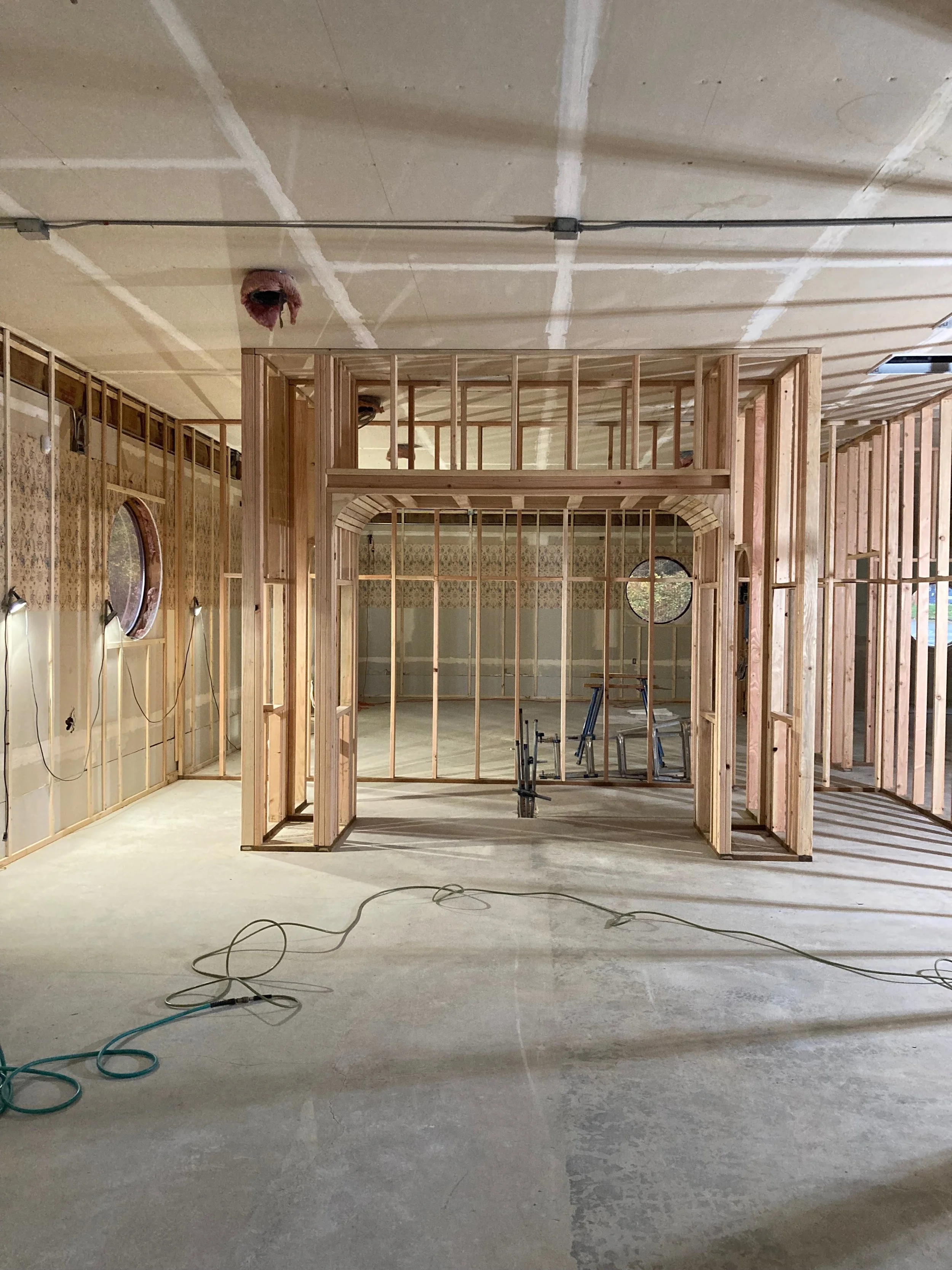 Interior of a building under construction with framed walls, unfinished ceiling, and exposed wiring and lighting fixtures.