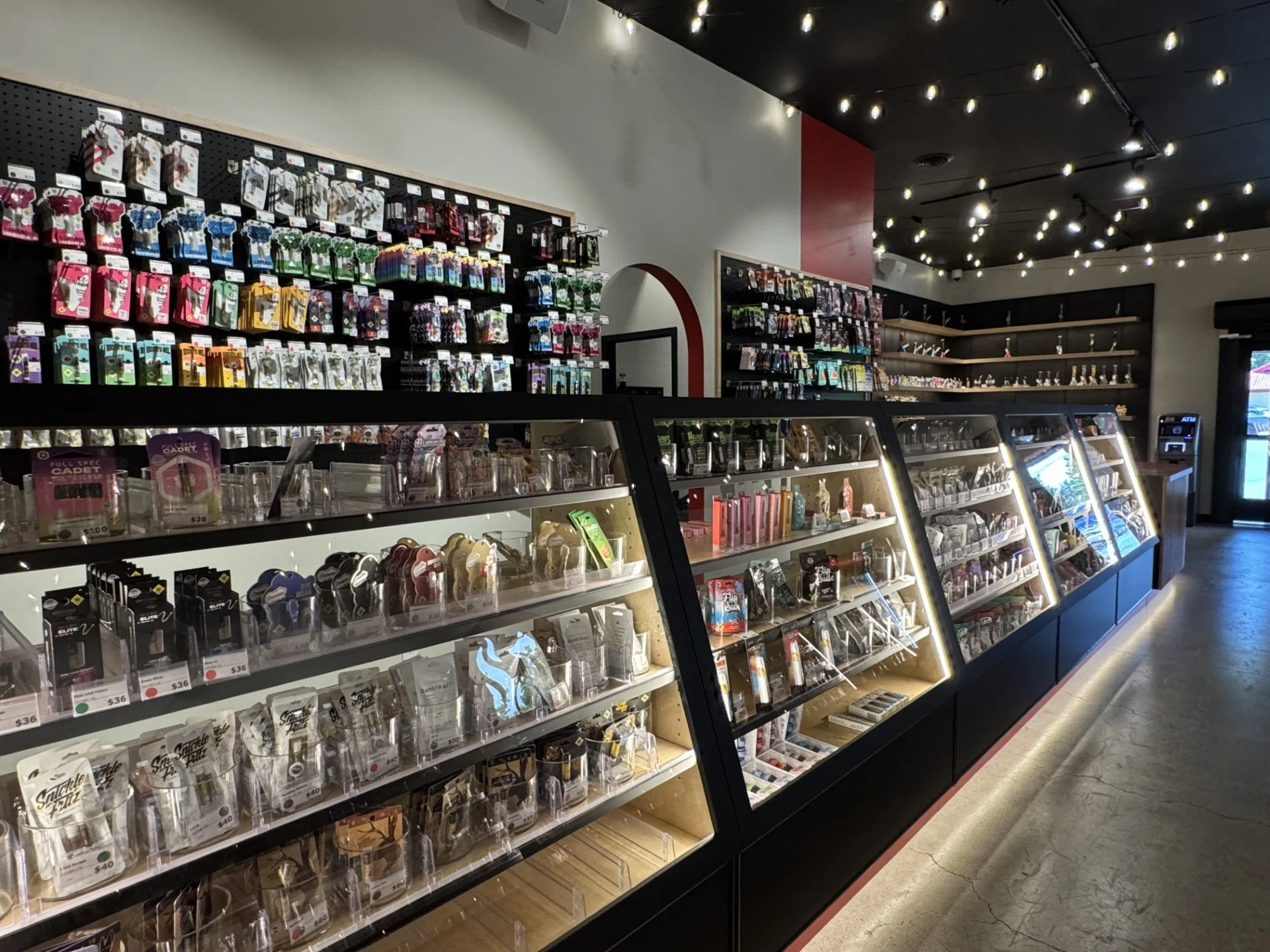 Inside a retail store displaying various candies and snacks in glass display cases and on wall shelves. String lights are hanging from the ceiling.