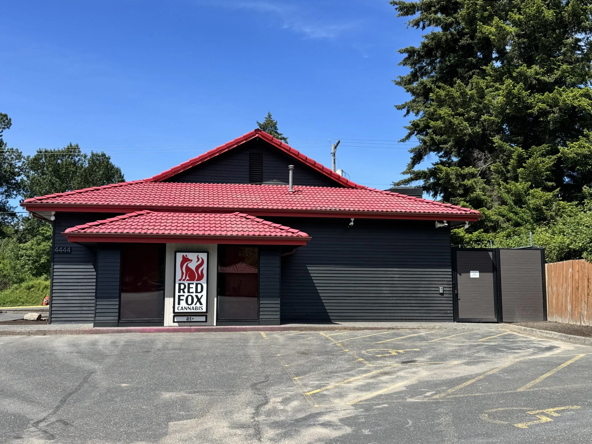 Front view of a black building with red tiled roof, signage for Red Fox Cannabis, and parking lot in foreground.