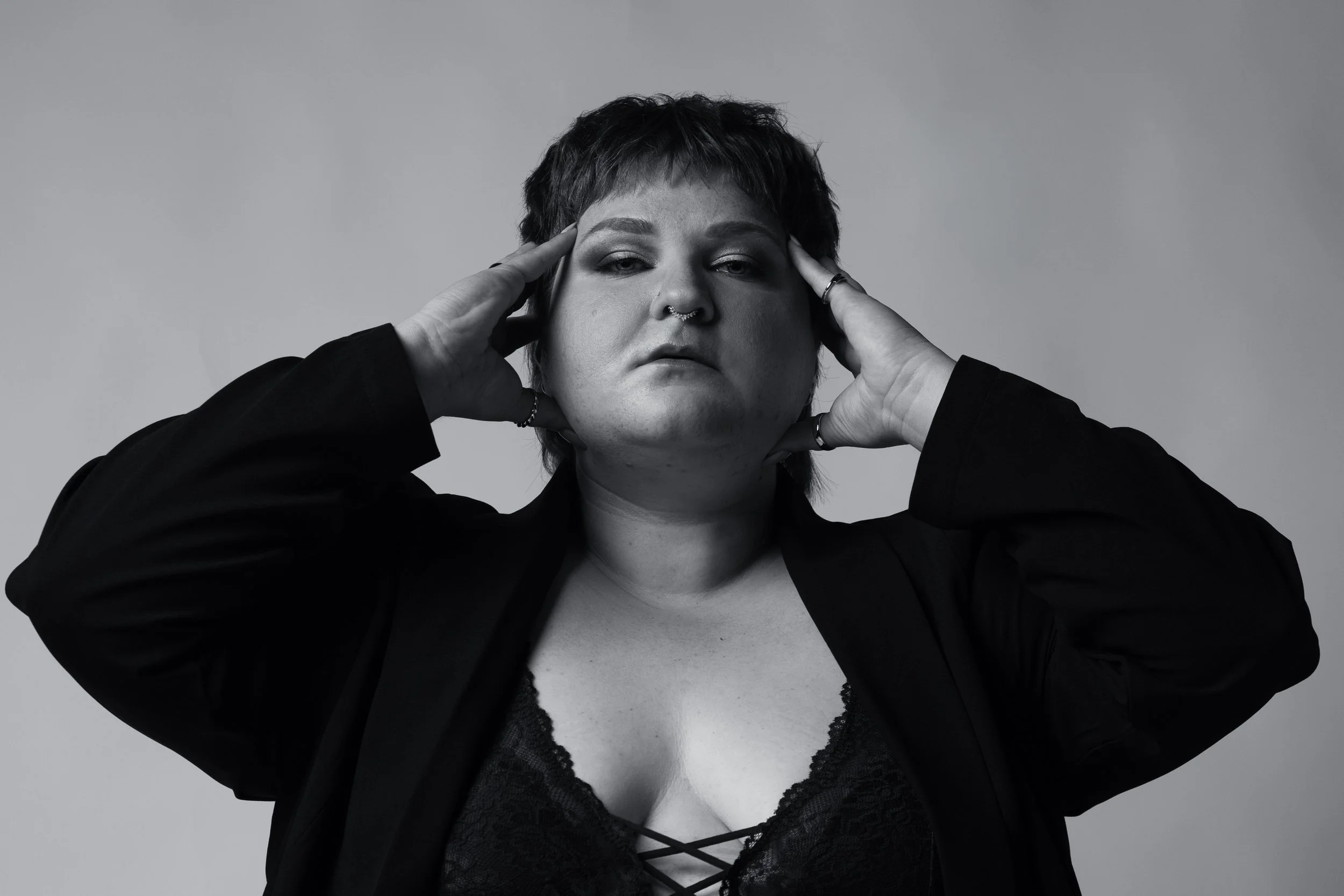 A close up black and white image of a woman with her hands on either side of her face looking directly into the camera