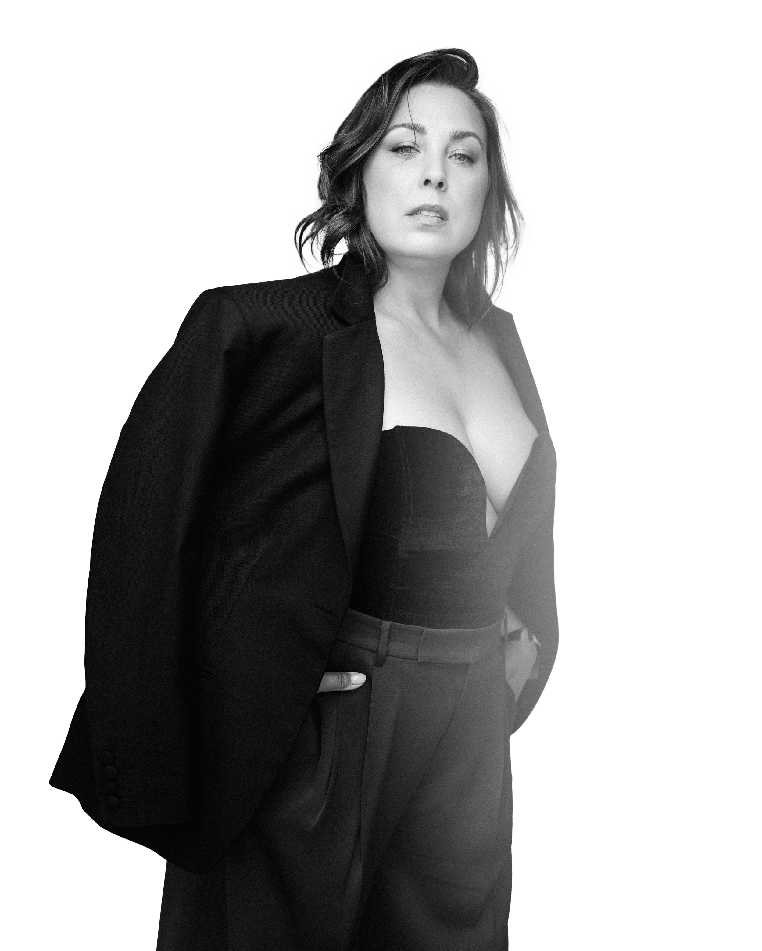 A black and white image of a woman standing powerfully, looking at the camera wearing a suit jacket draped over her shoulders