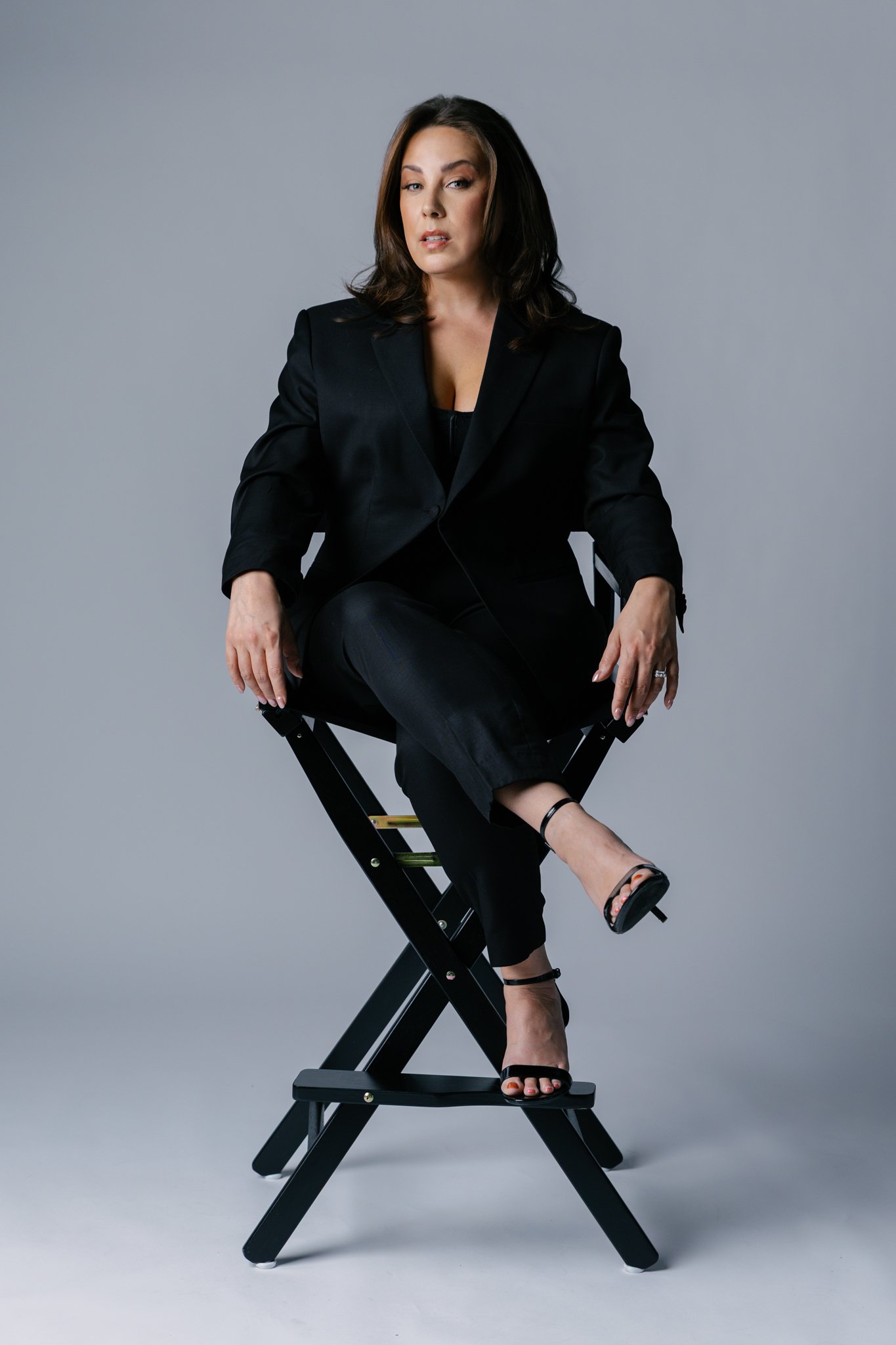 Chantelle sitting on a director's chair wearing a black suit staring directly at the camera in moody lighting