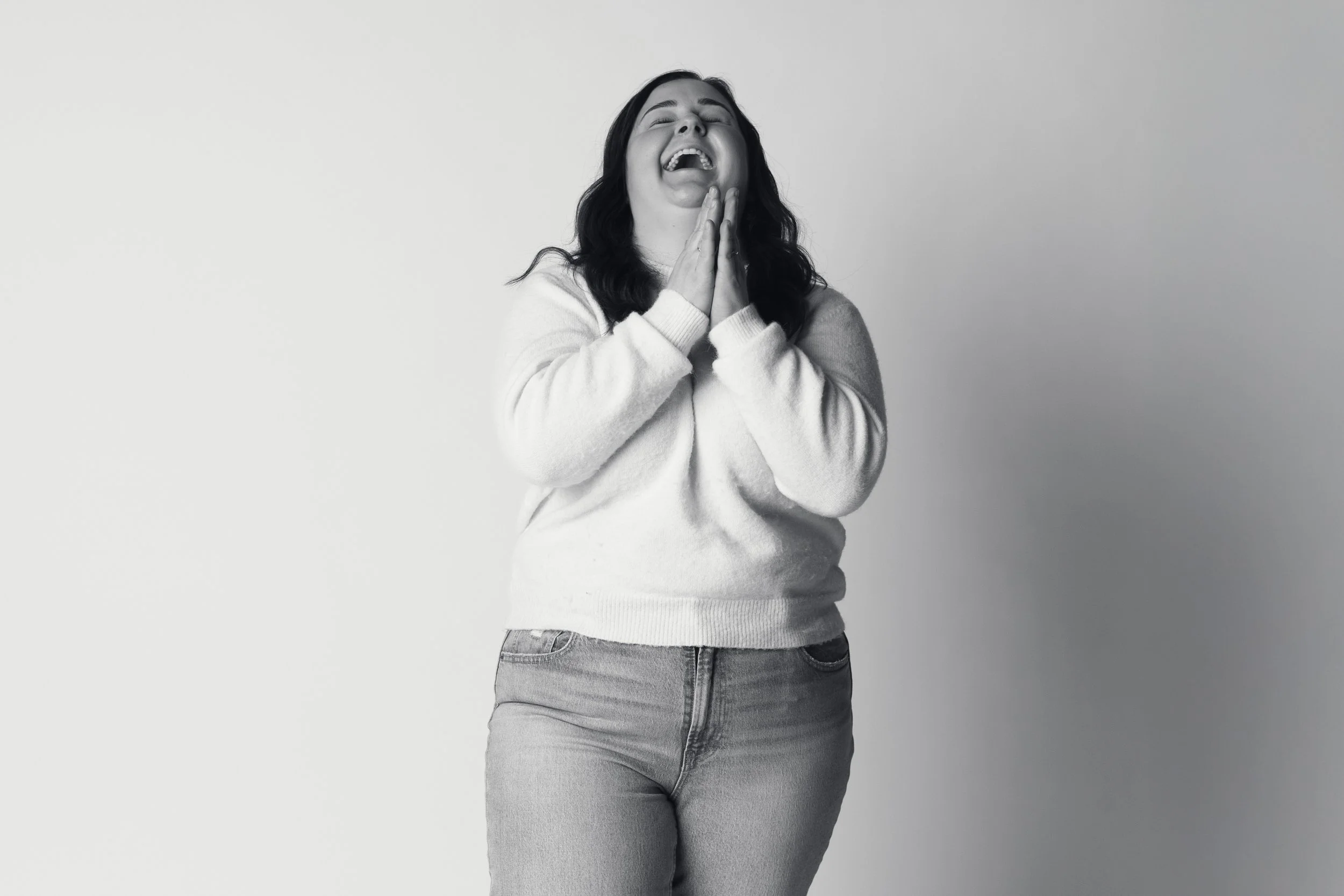 A black and white image of a plus size woman laughing with her hands in a prayer-like pose
