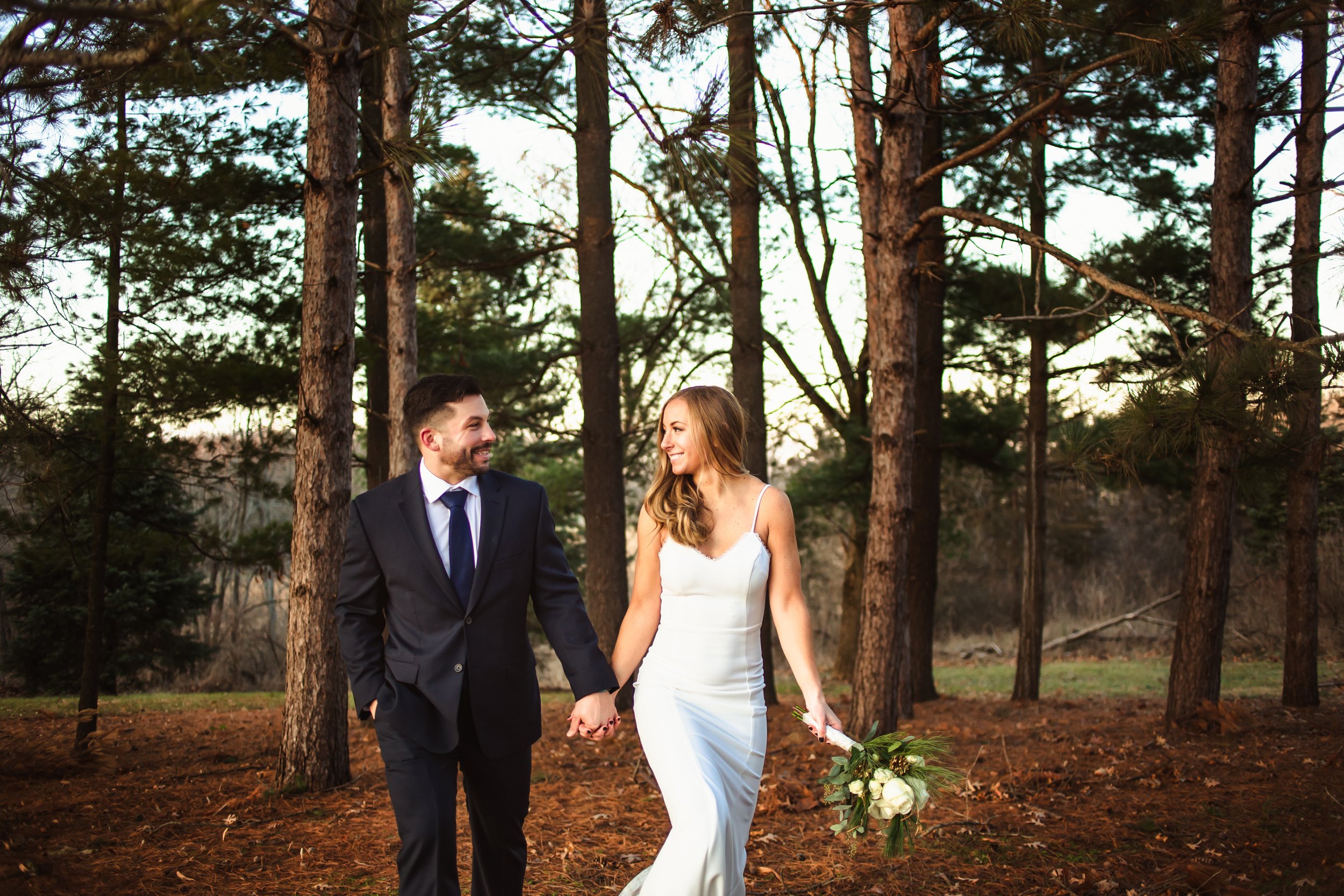  Newlyweds walk hand in hand through a wooden forest at dusk captured by Teala Ward Photography. bride and groom portraits Ironwood Illinois #tealawardphotography #tealawardweddings #LaSalleIllinois #IronwoodontheVermillion #weddingphotographyIL 